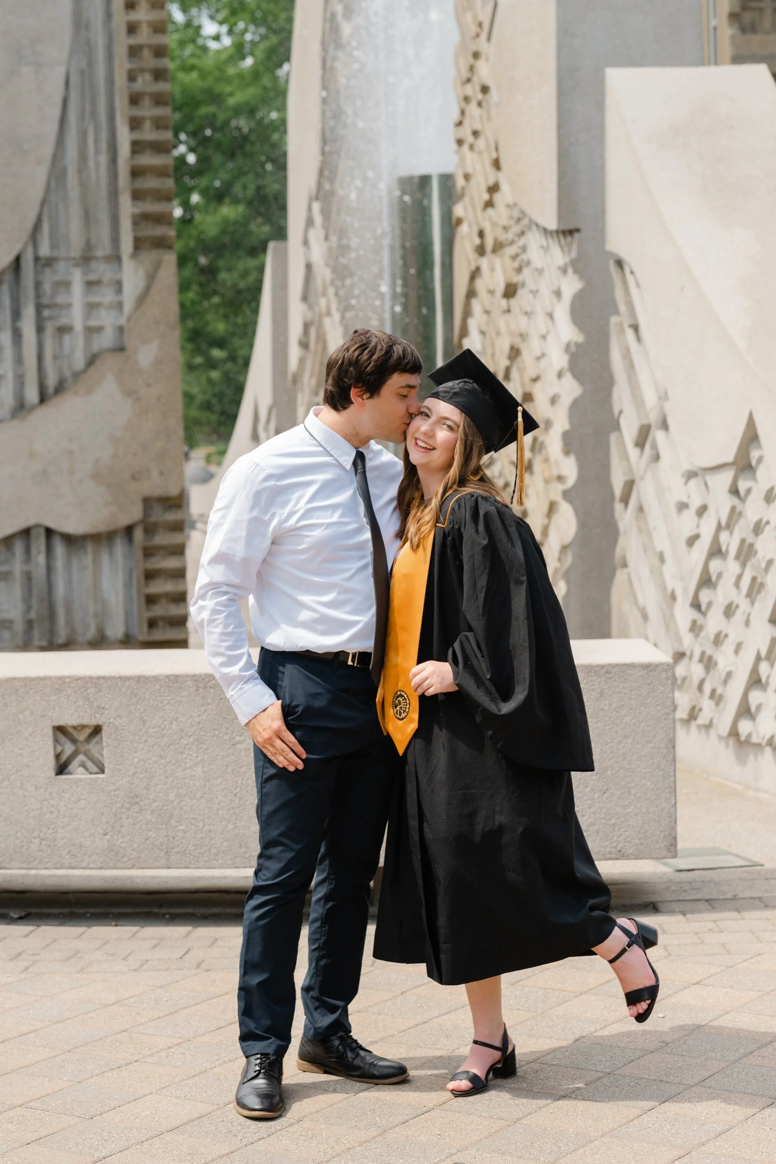 Man kissing woman wearing purdue graduation cap and gown standing in front of the engineering fountain,