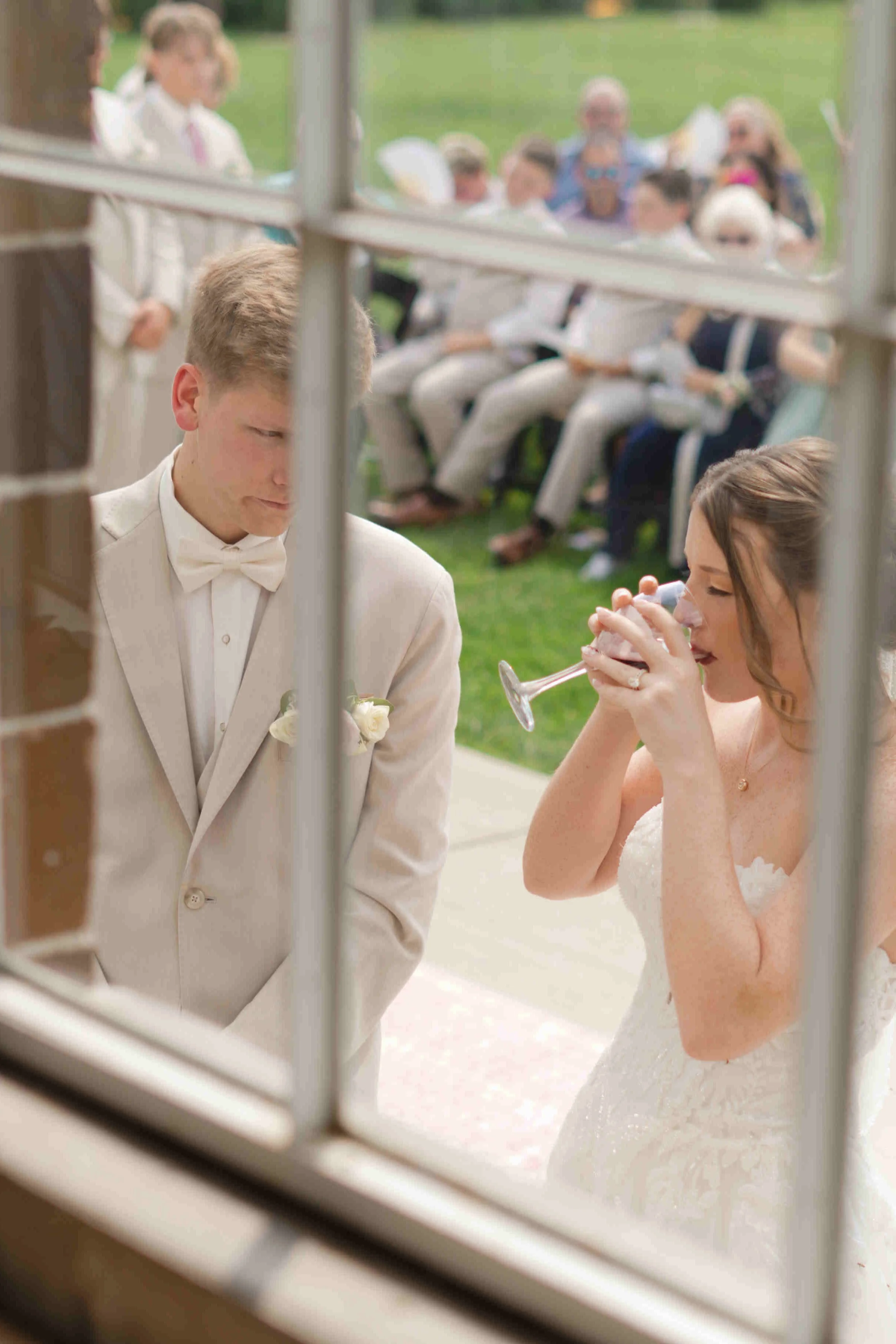 looking through the window at Blossom barn at the bride and groom taking Holy Communion during their outdoor wedding ceremony.