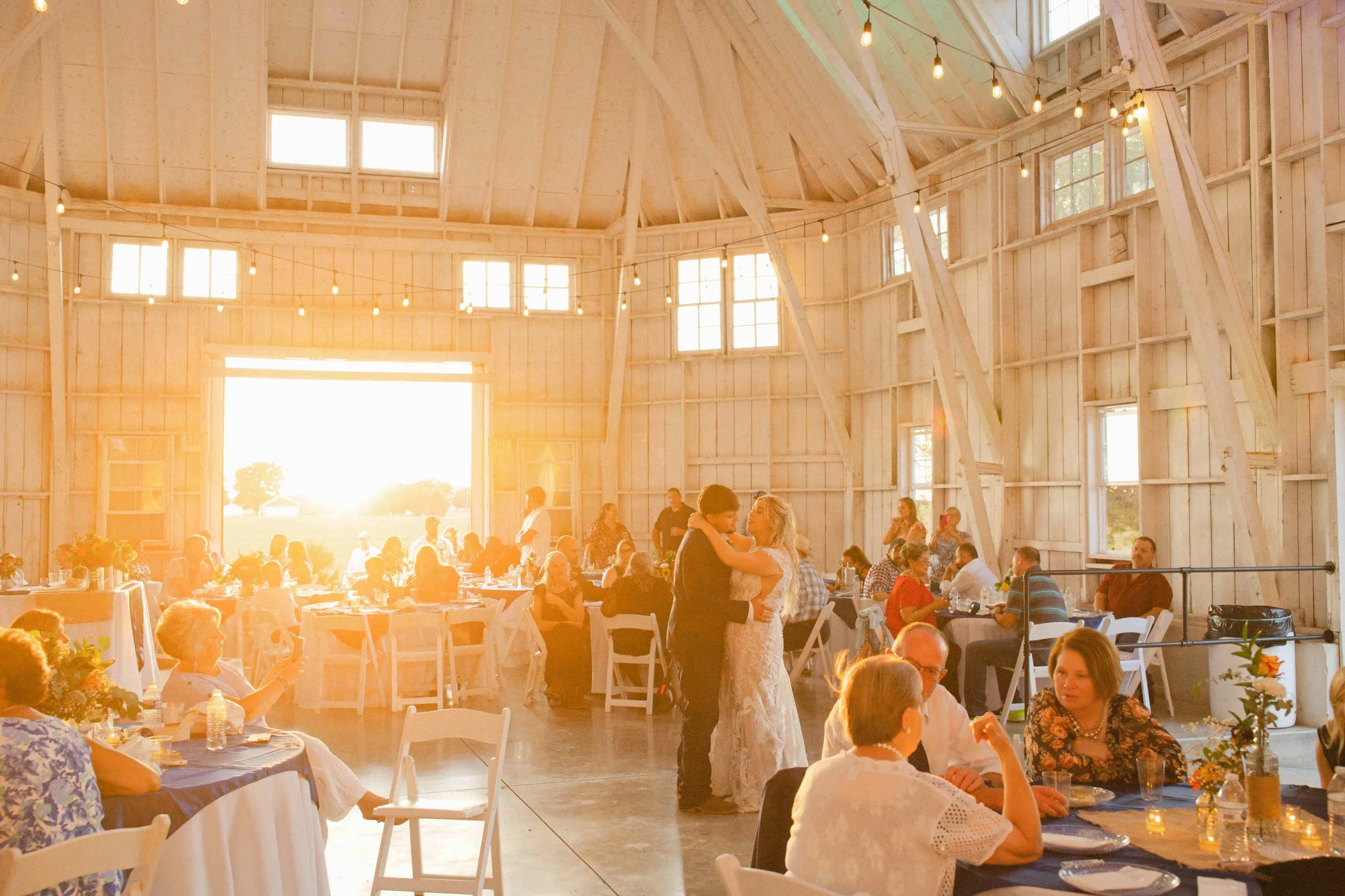 The sun setting is casting warm glowing light through the big barn doors of Governor's Pavilion wedding barn as the bride and groom dance their first dance as husband and wife.  Photo by Heather Corbin Photography