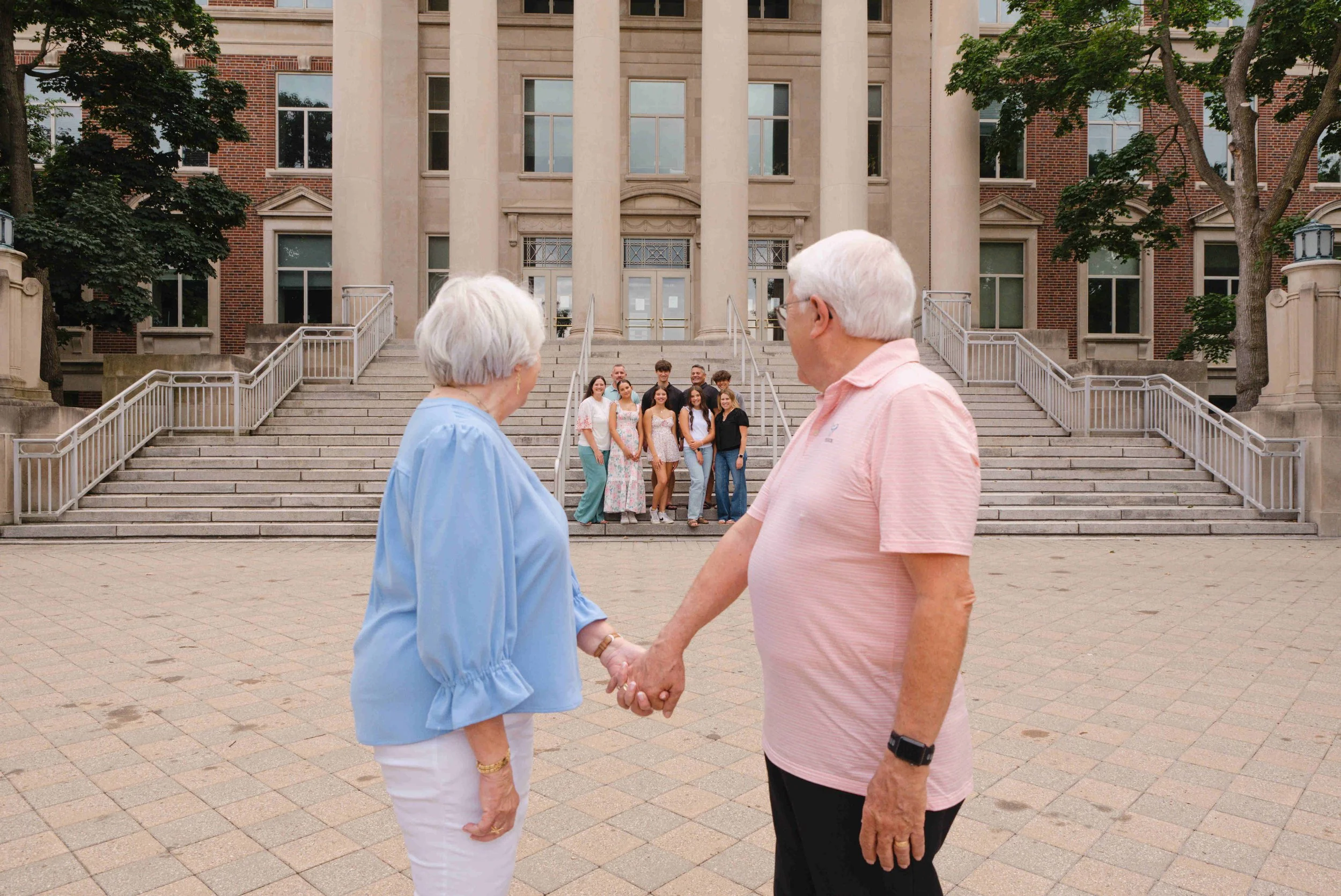 Grandparents holding hands looking back at their kids and grandchildren.  3 generation photo at Purdue University in front of Hovde Hall