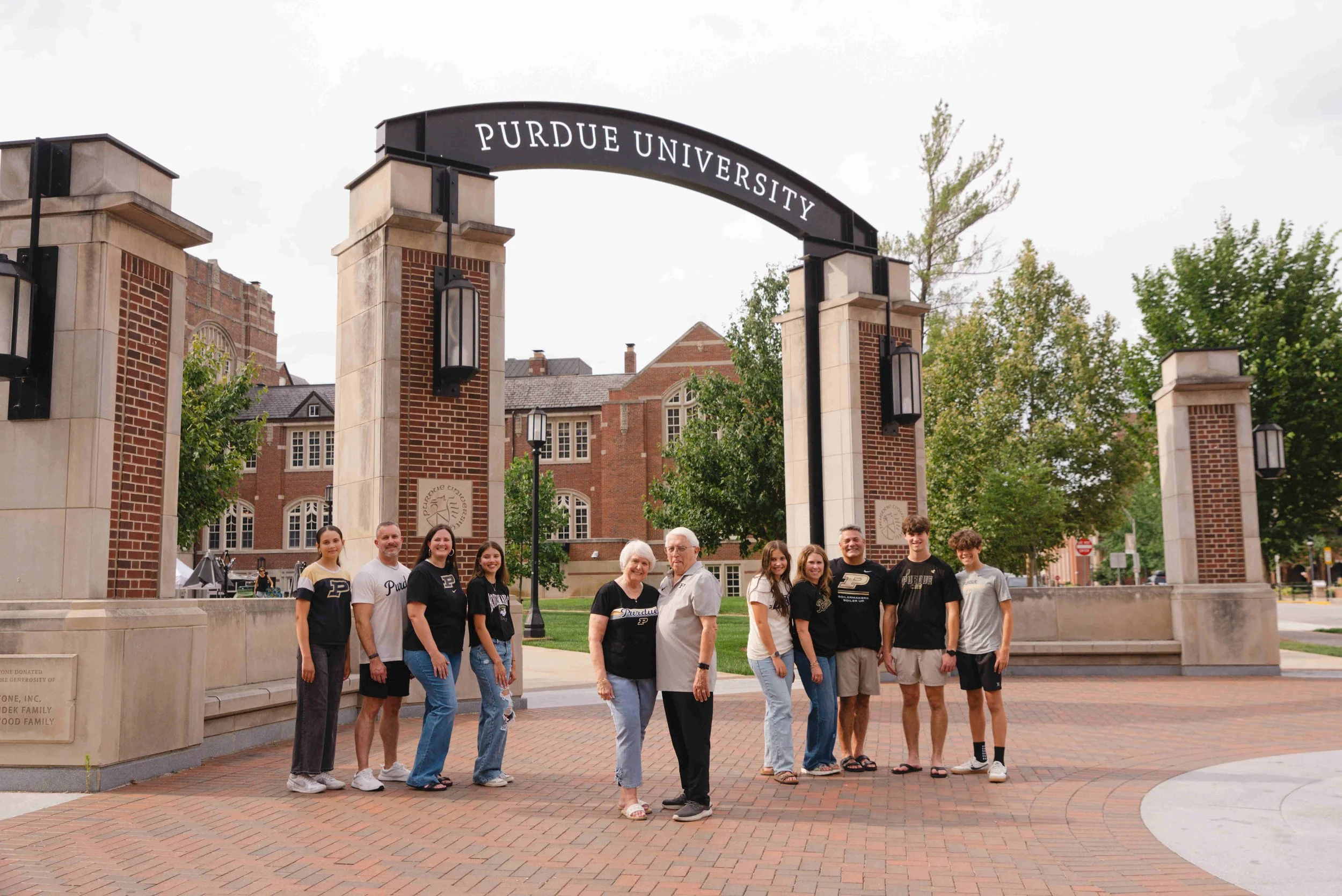Grandparents standing together with their children's families behind them in front of the Purdue Arch by the Union.