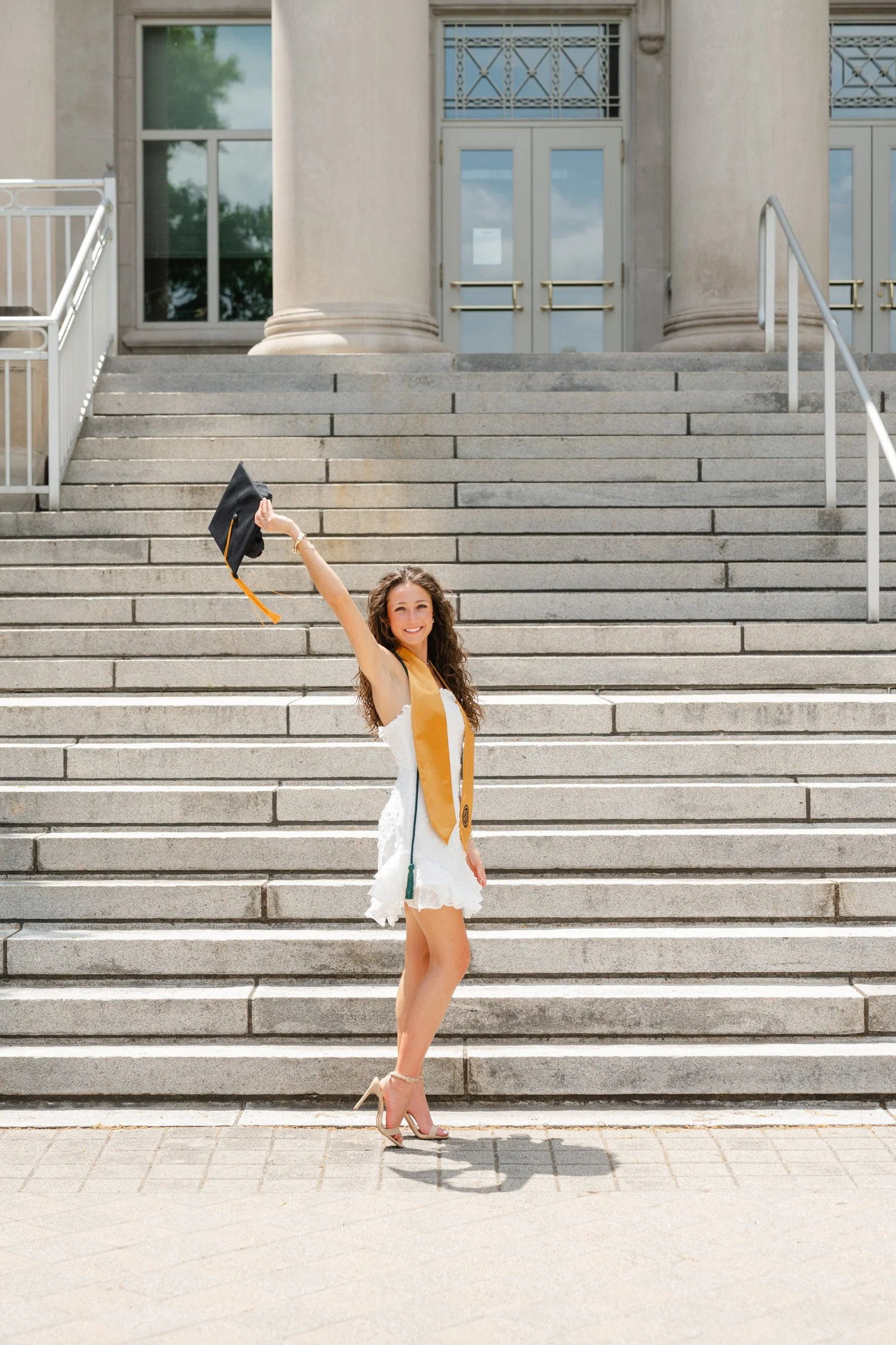 Purdue grad in white dress tossing her graduation cap in front of the hovde hall steps at Purdue University photo by heather corbin photography