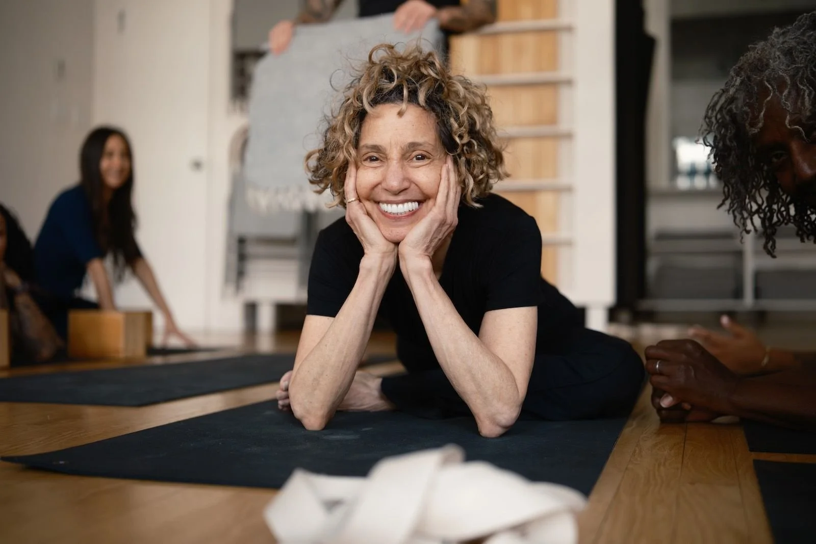 A woman with curly hair smiling while on a yoga mat at a yoga class for Katonah Yoga training in Puerto Vallarta.