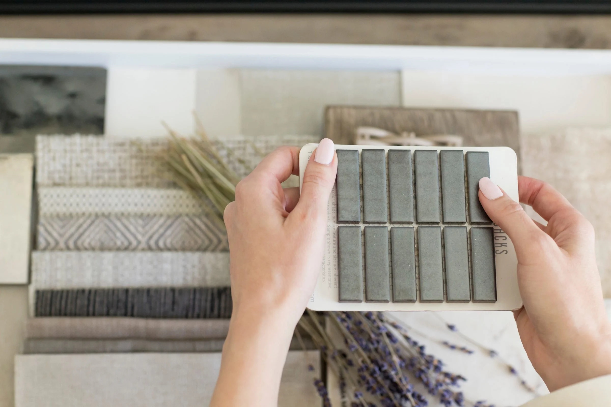 Person holding a tile sample card over a display of various tile materials.