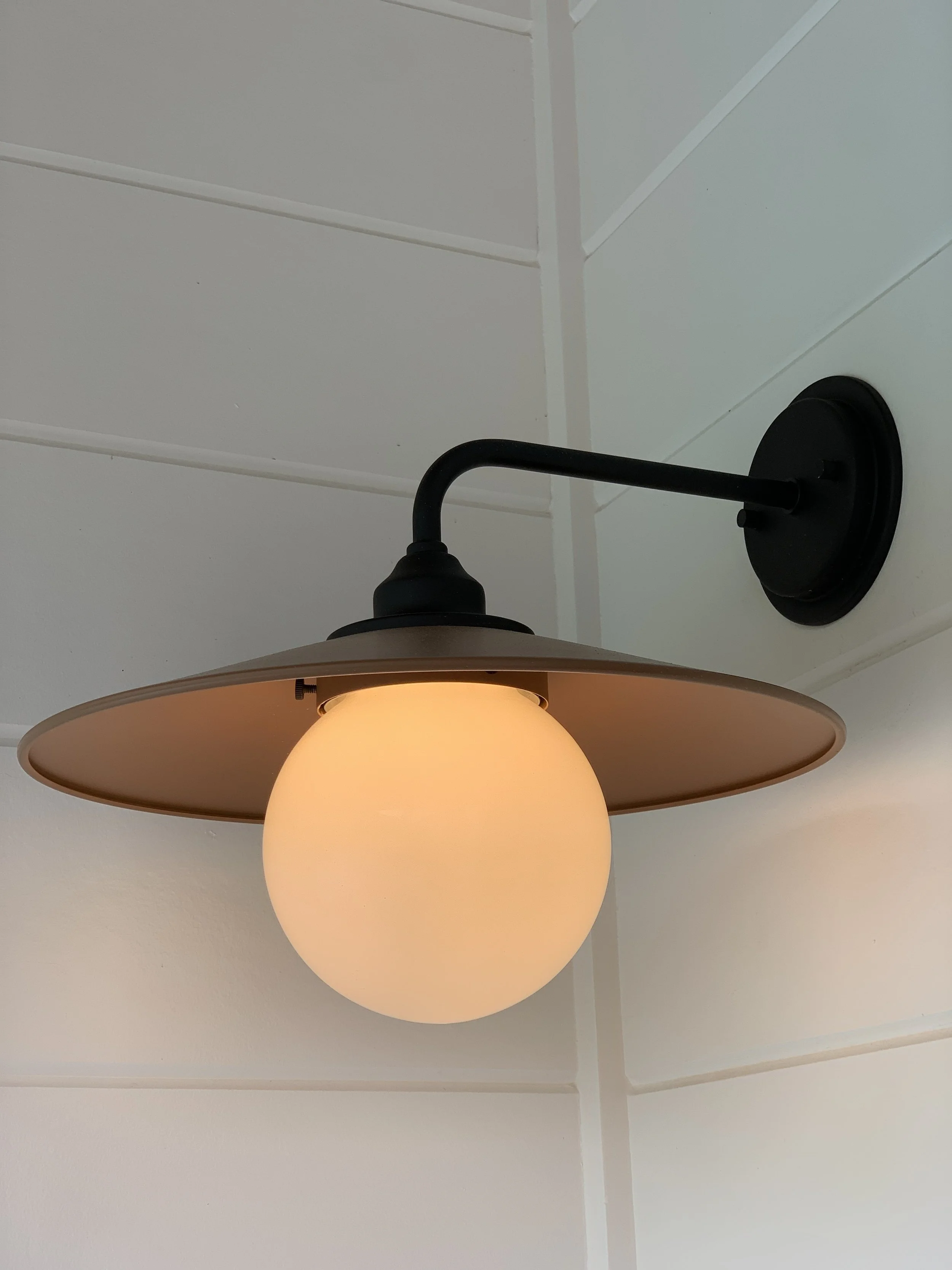 Ceiling light fixture with a large opaque glass globe, black arm, and mount, mounted on a white ceiling with visible panels.