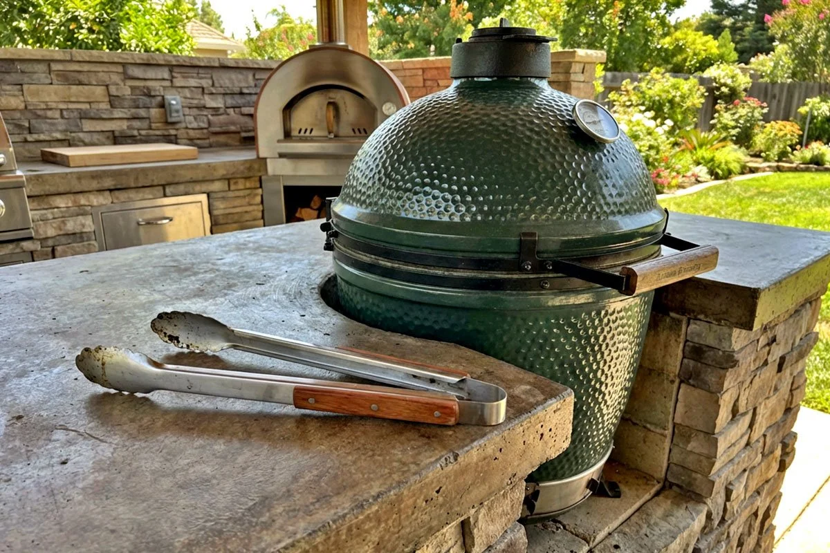 Kamado grill and tongs in an outdoor kitchen.