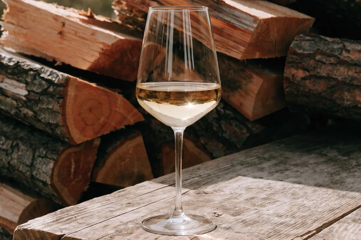 Glass of white wine in front of split hardwood.