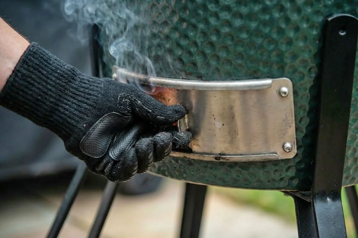 Adjusting the vent on a kamado smoker grill.