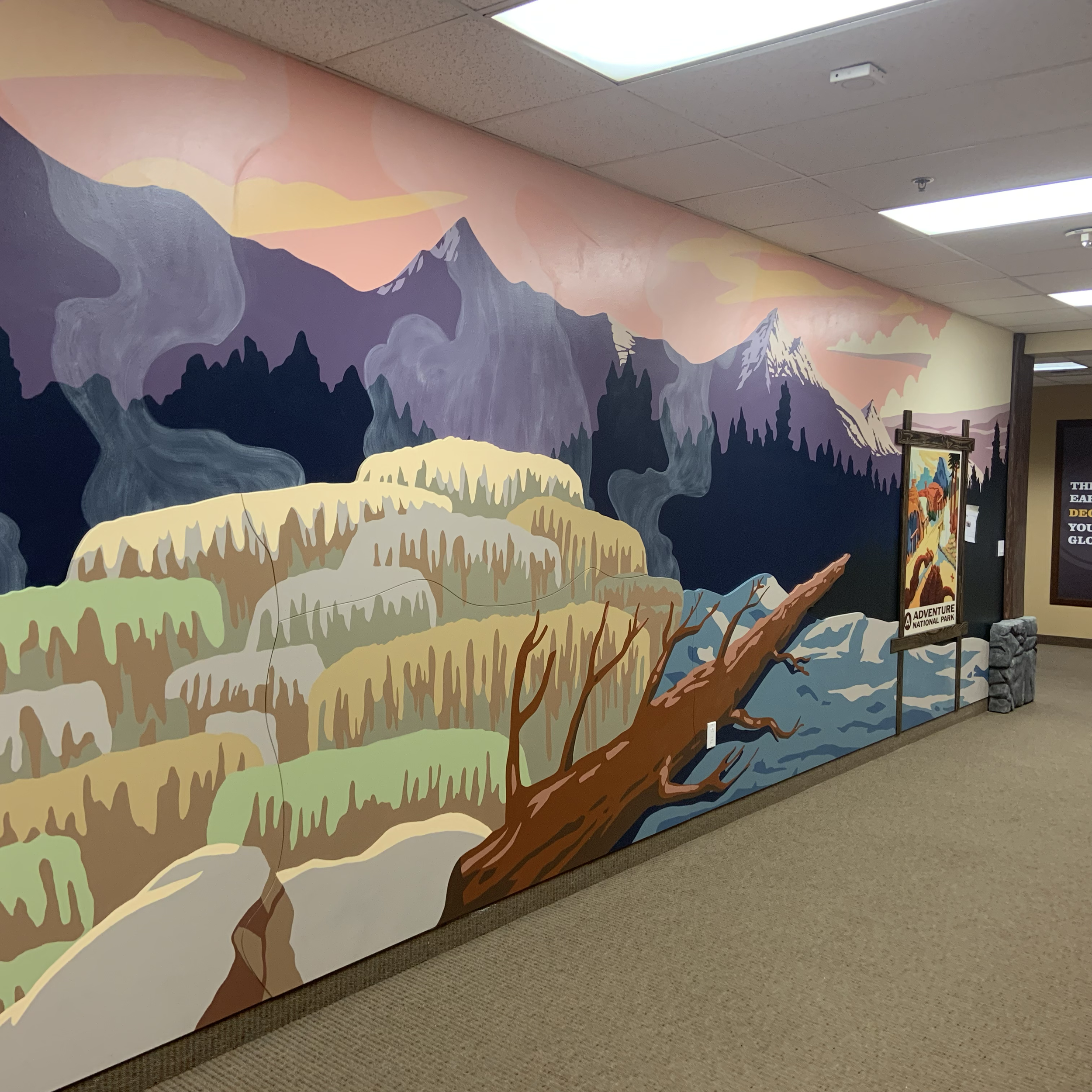 Colorful mural of mountains, trees, and a fallen log in an indoor setting with a small person in the distance.