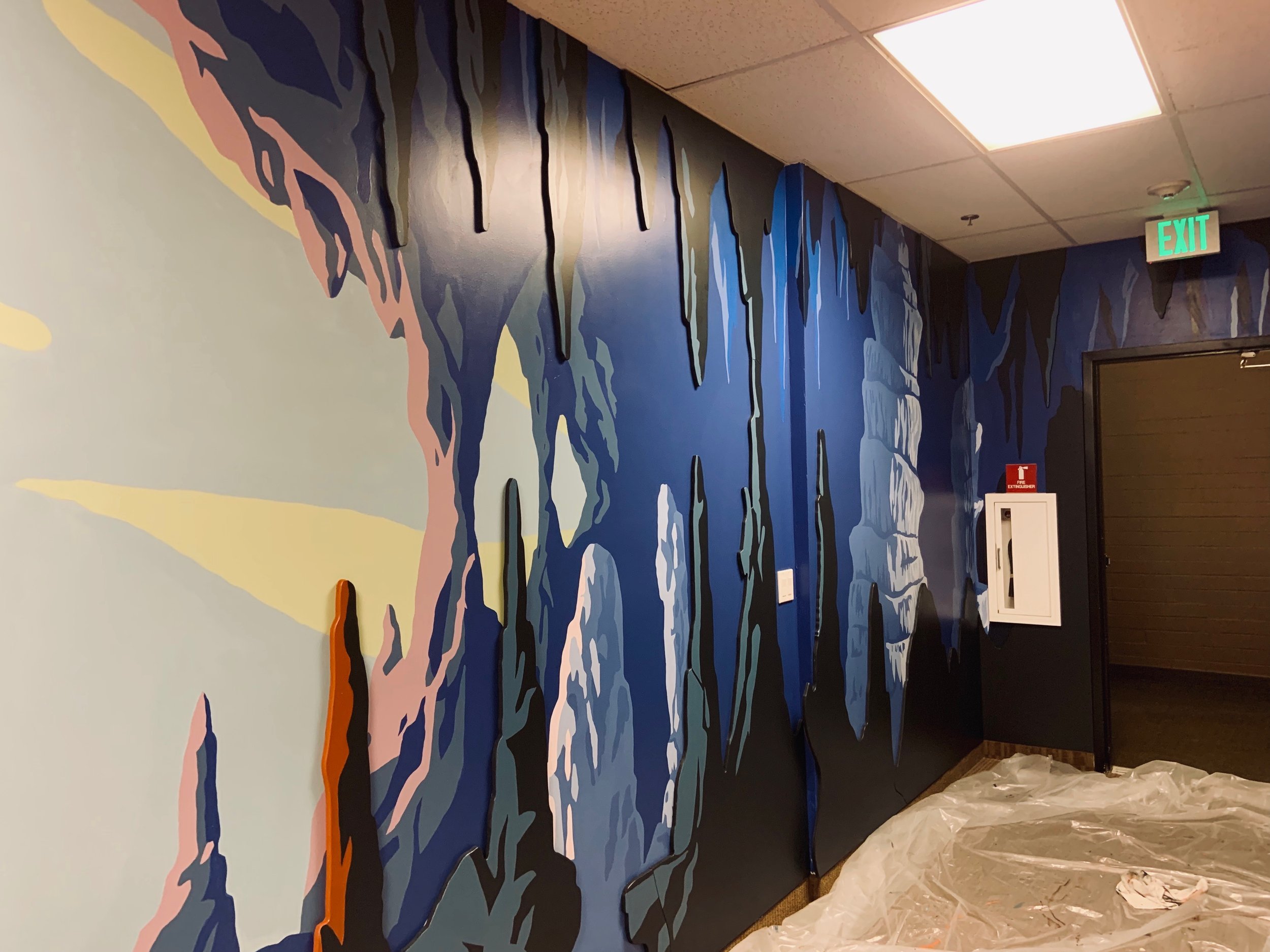 Painted cave with stalactites and stalagmites in shades of blue, gray, and black, with some pink and orange accents.