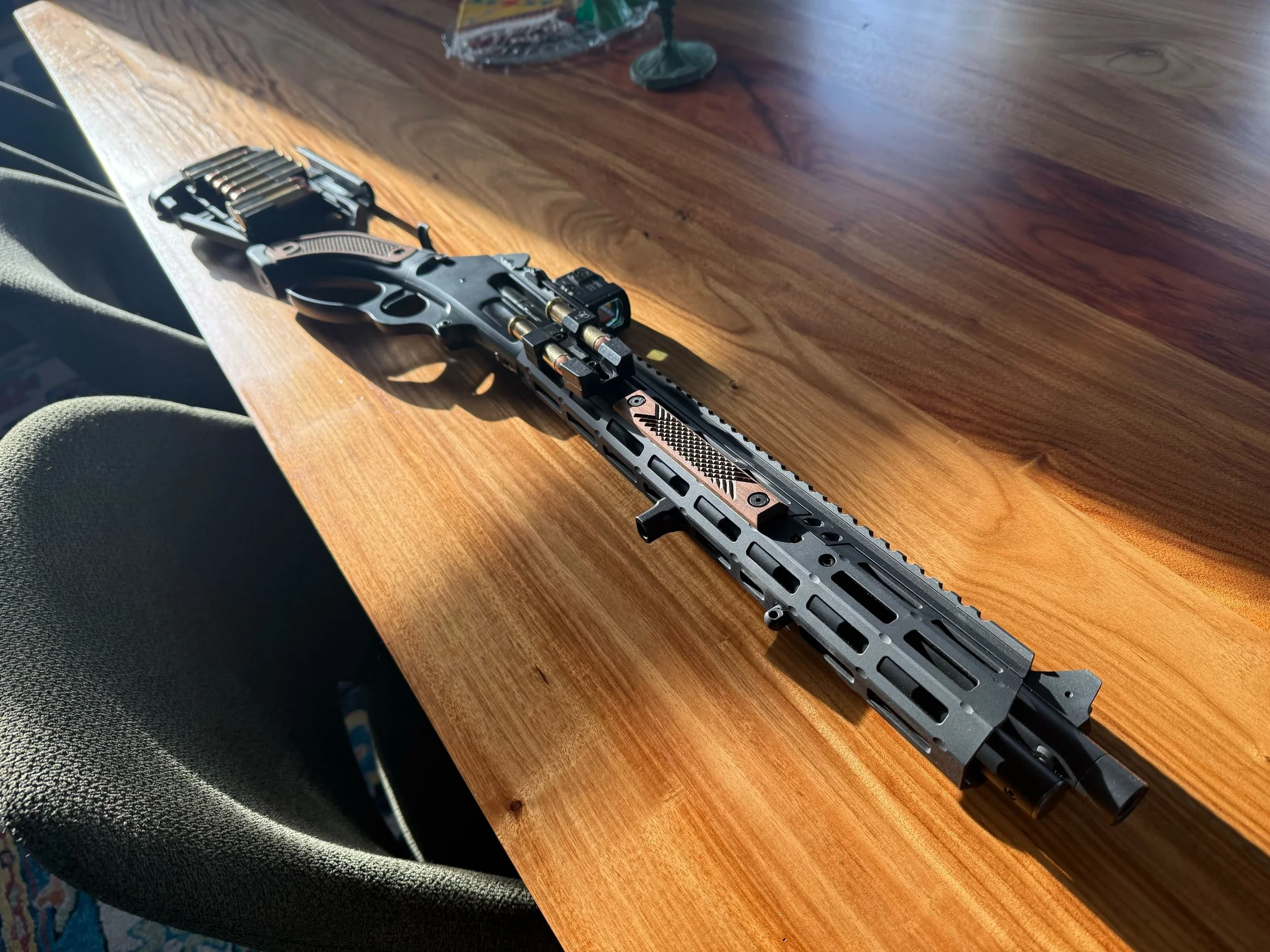 A black and copper rifle with a scope and tactical accessories resting on a wooden table.