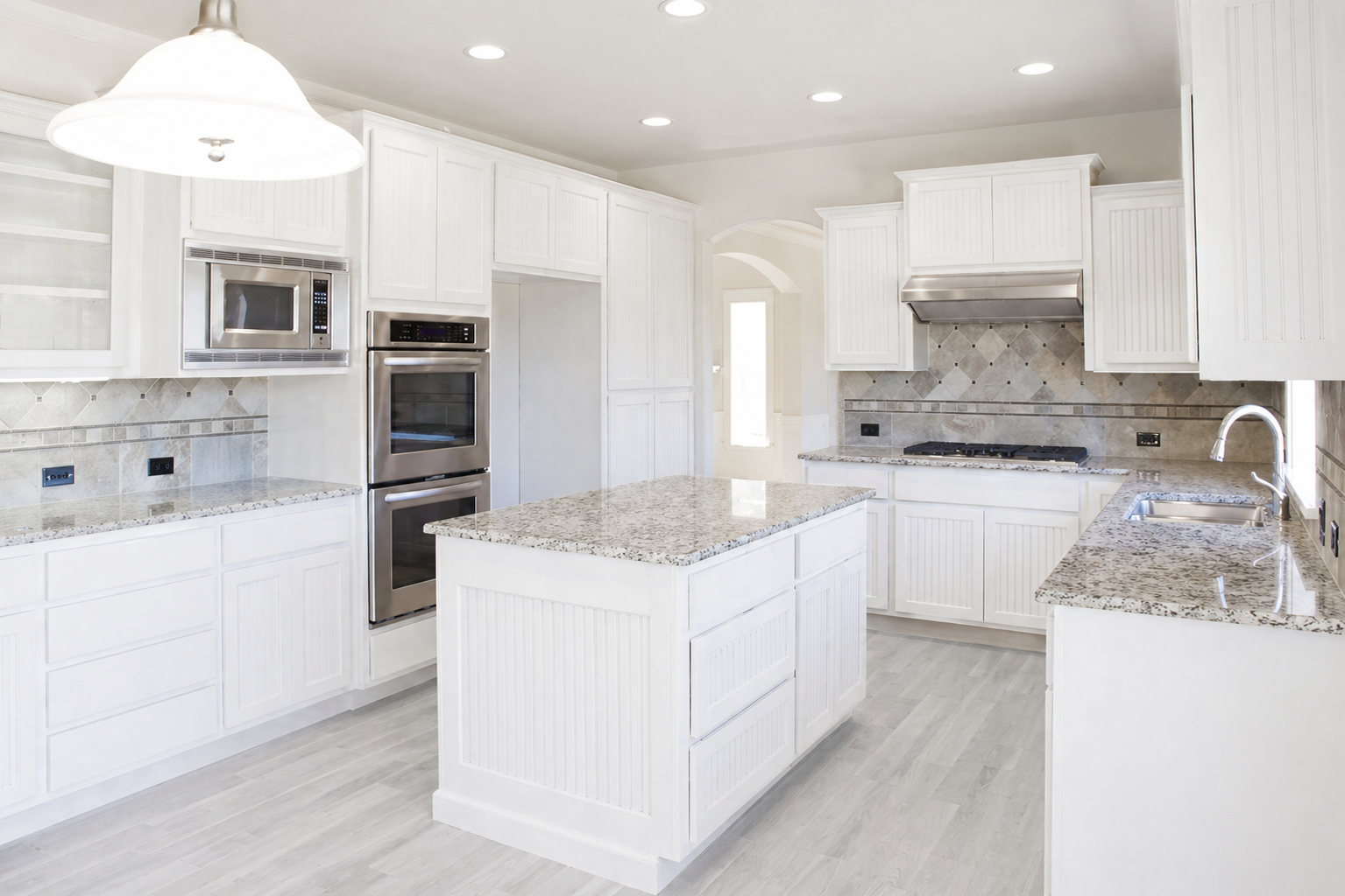 Bright, modern kitchen with white cabinets, granite countertops, stainless steel appliances, and a kitchen island.
