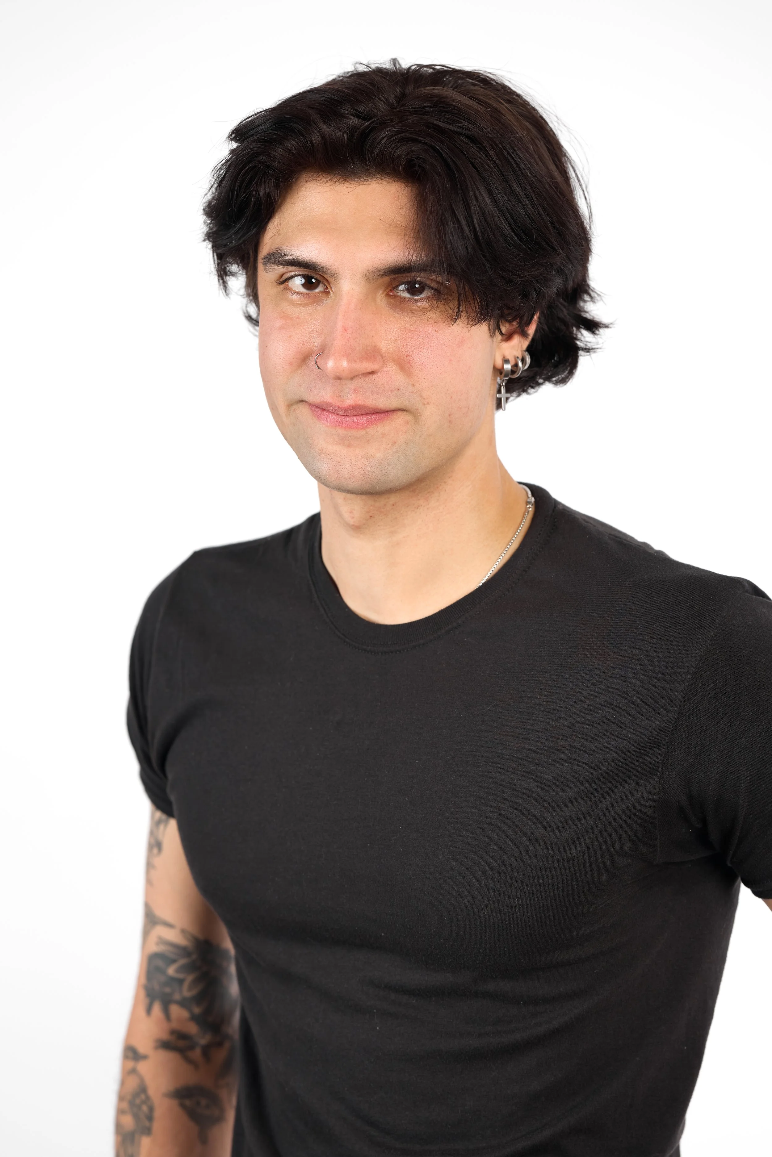 Chicago Modelling Digital of a young man with dark, wavy hair wearing a black t-shirt and jewelry, posing against a white background.