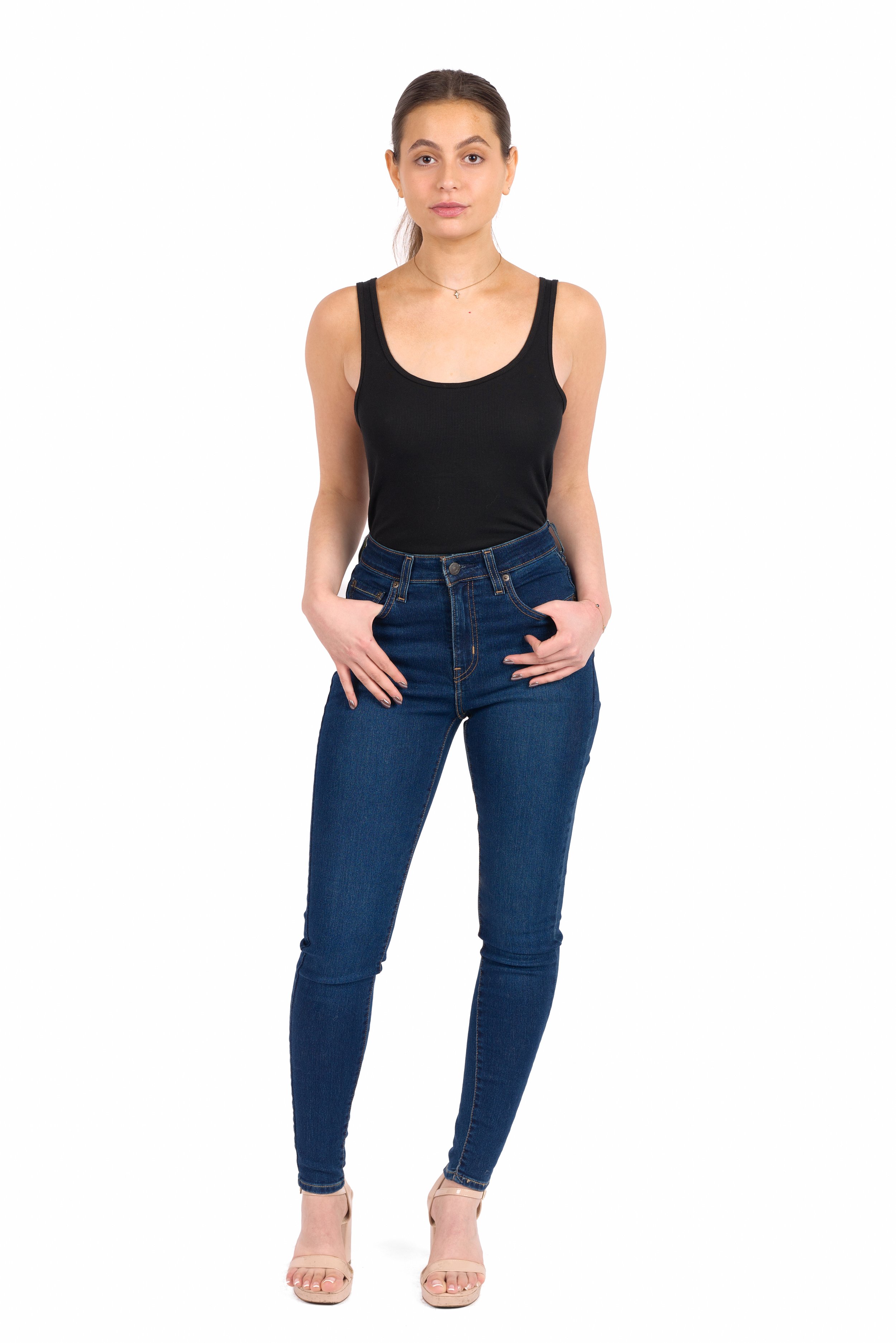 Chicago Modelling Digital of a young woman in a black tank top, dark blue jeans, nude heels, standing with her hands in her pockets, against a white background.