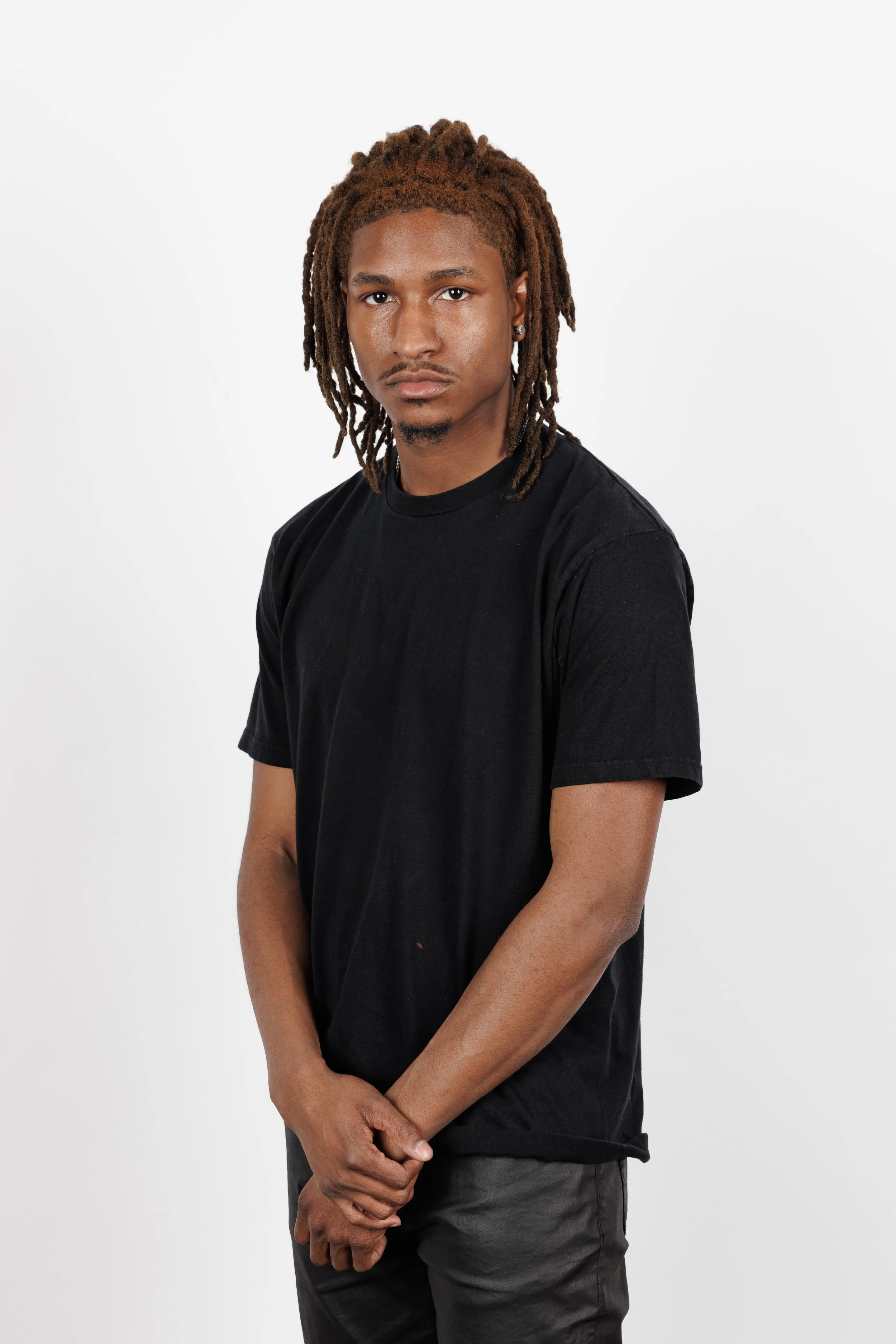 Chicago Modelling Digital of a young man with dreadlocks wearing a black t-shirt and dark pants, standing against a white background.