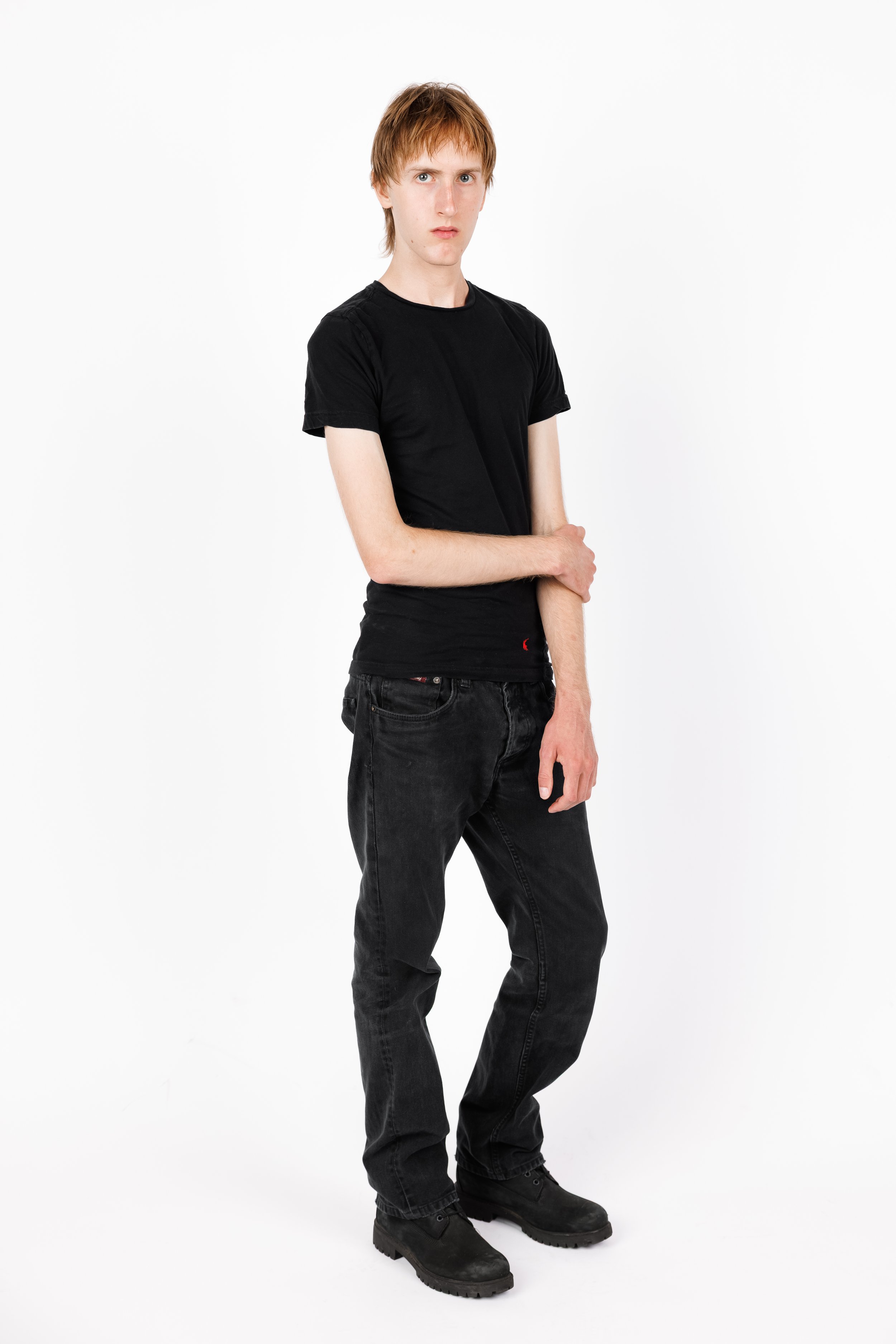 Chicago Modelling Digital of a young man with light skin and reddish-brown hair, wearing a black t-shirt, black jeans, and black boots, standing against a plain white background.