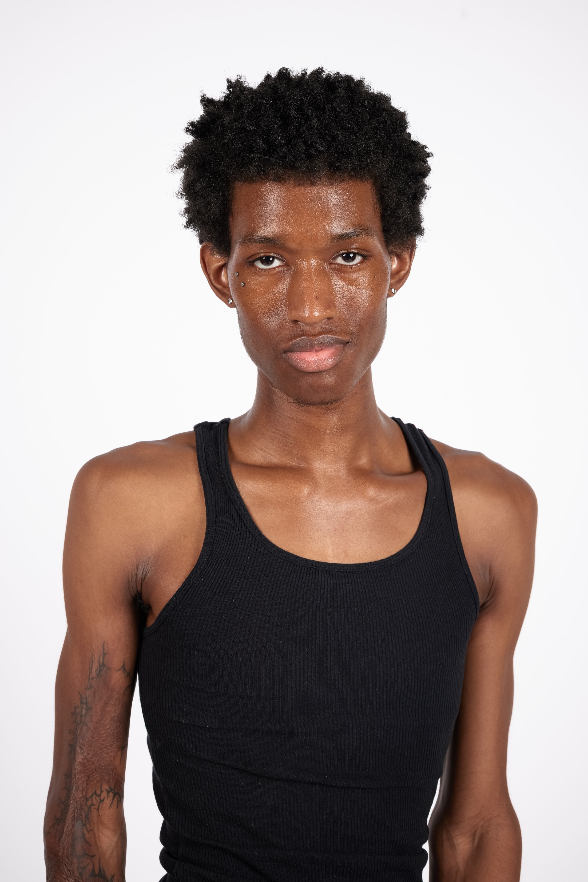 Chicago Modelling Digital of a young man with short curly hair wearing a black sleeveless top and small earrings against a white background.