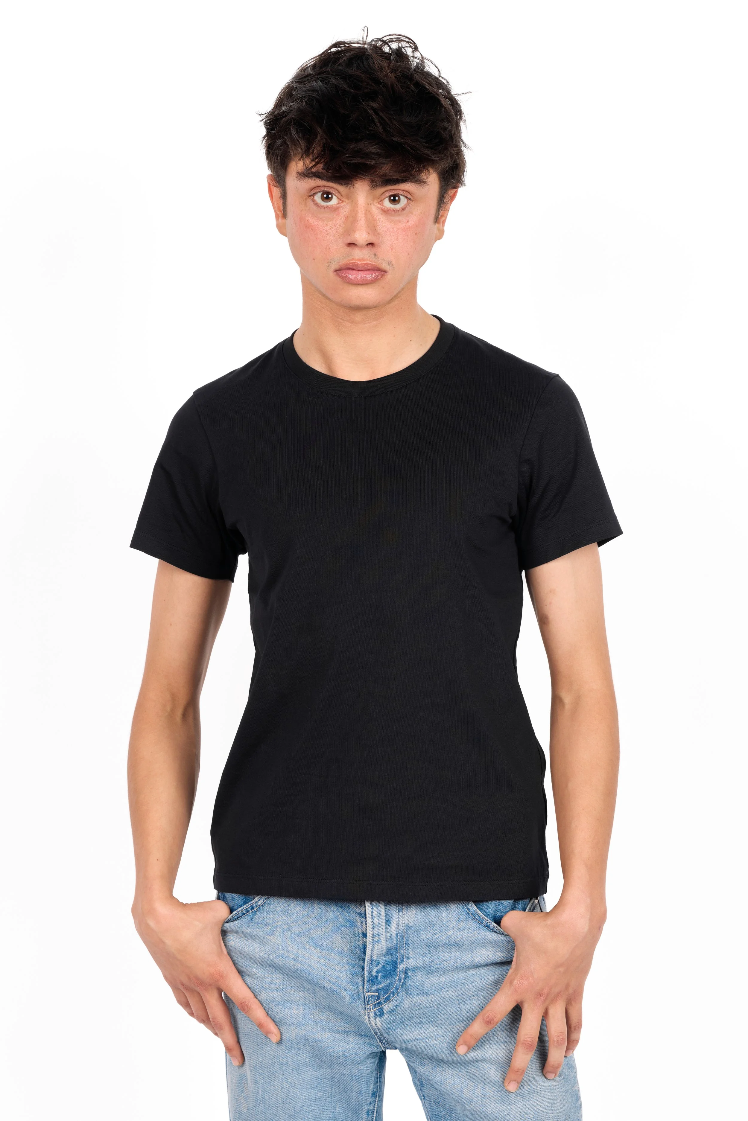 Chicago studio modeling digitals of a man withshort, curly dark hair wearing a black T-shirt and light blue jeans, standing against a white background.