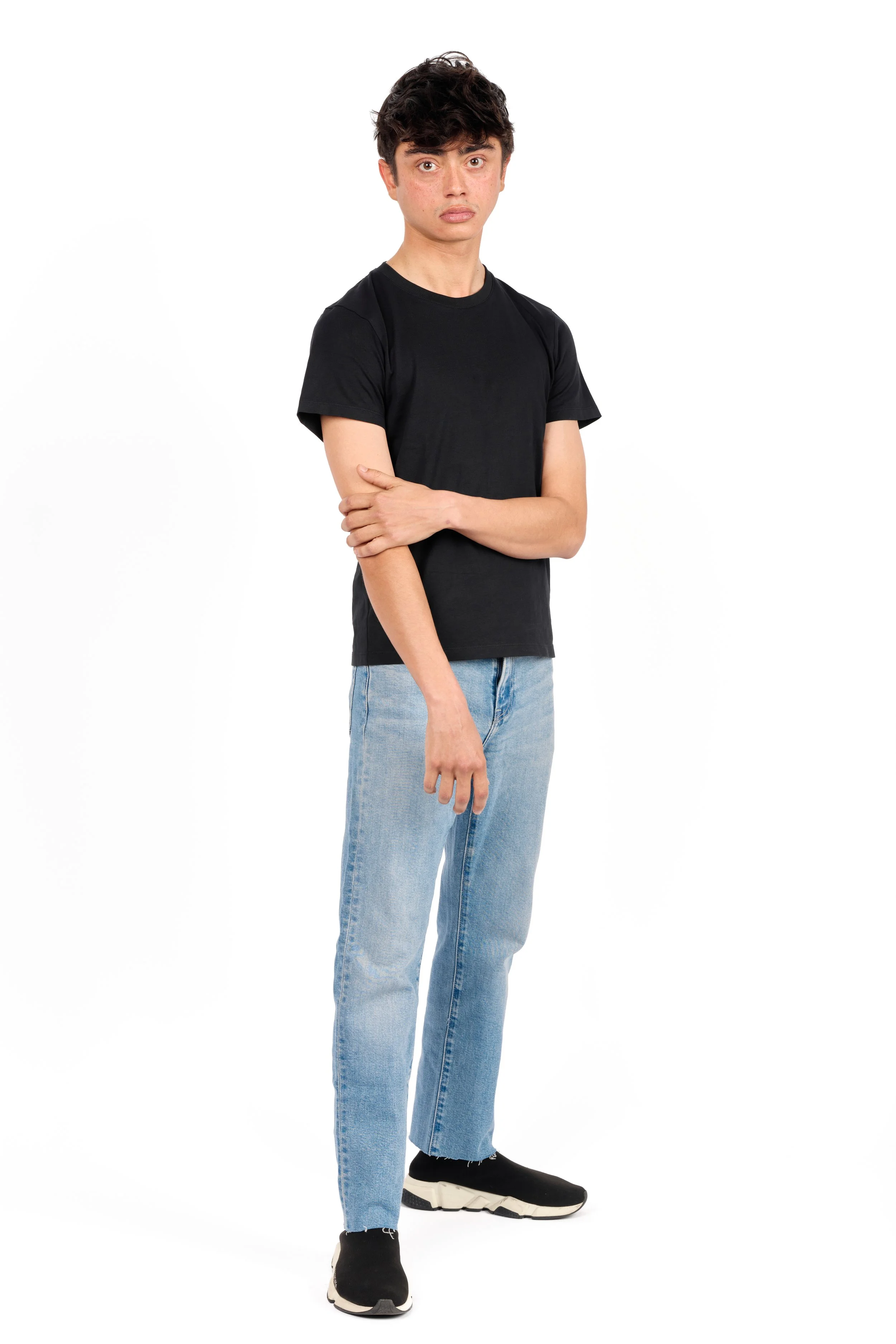 Chicago studio modeling digitals of a man with dark hair wearing a black t-shirt, light wash jeans, and black sneakers, standing against a white background.