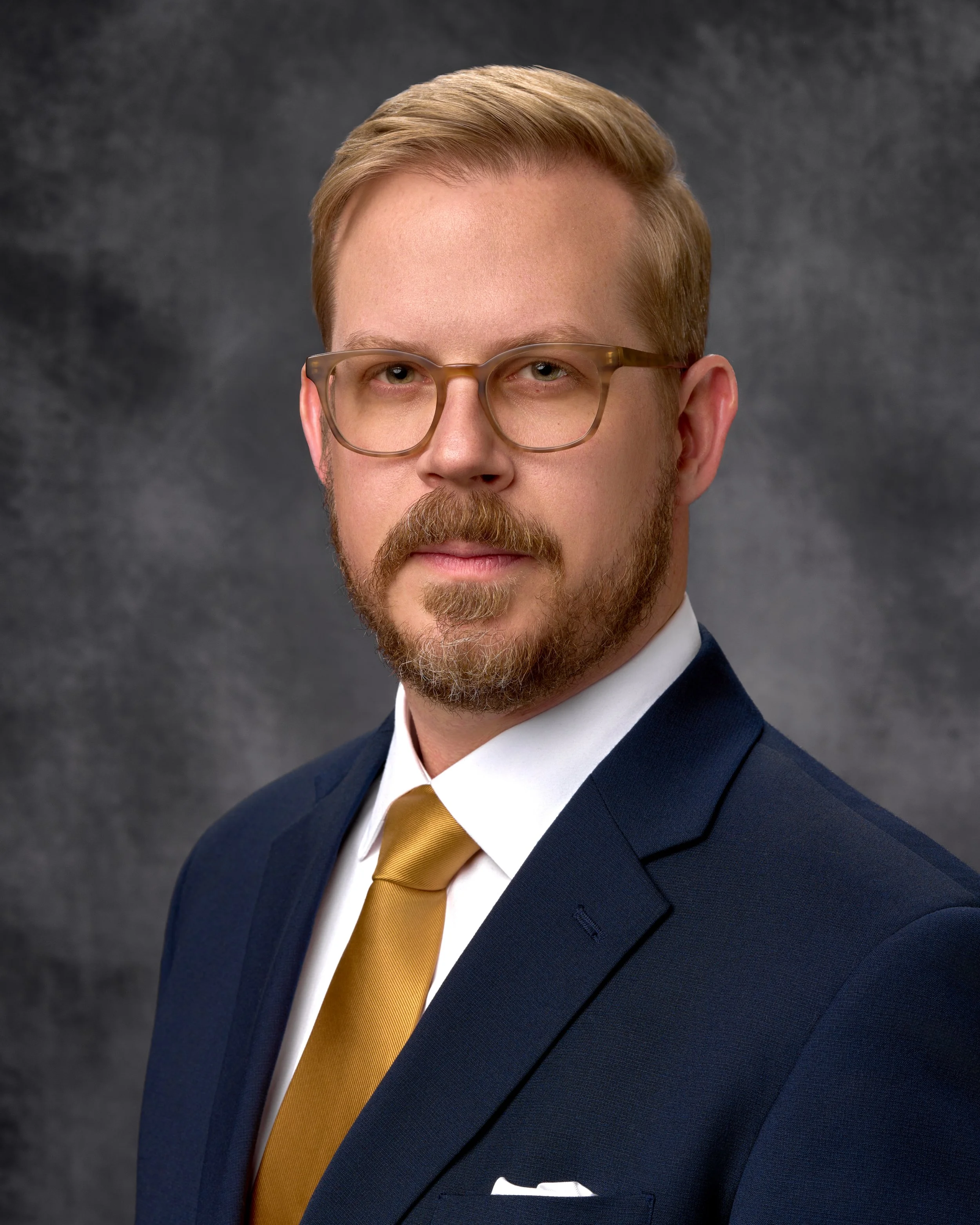 Chicago professional headshot portrait of a corporate man with glasses, a beard, wearing a navy suit, white shirt, and gold tie.