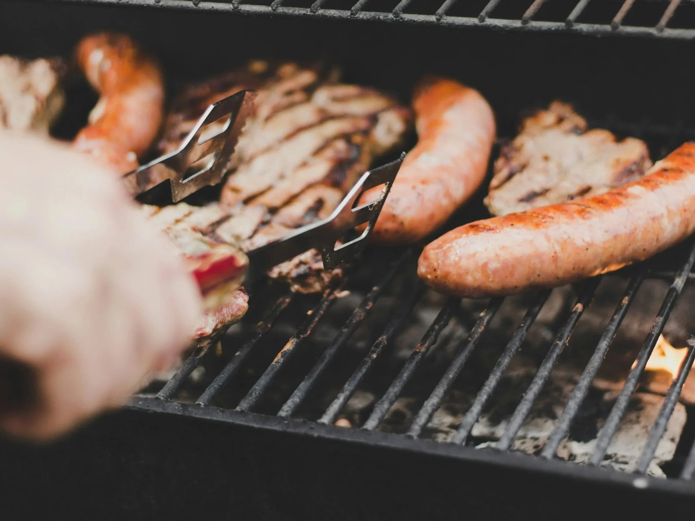 Sausages and meat grilling on a barbecue grill over an open flame.