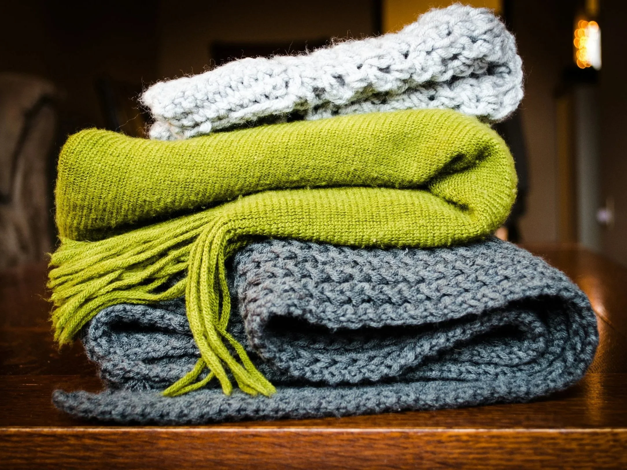 Stacked folded knit sweaters in gray, yellow, and multicolored yarns on a wooden surface.