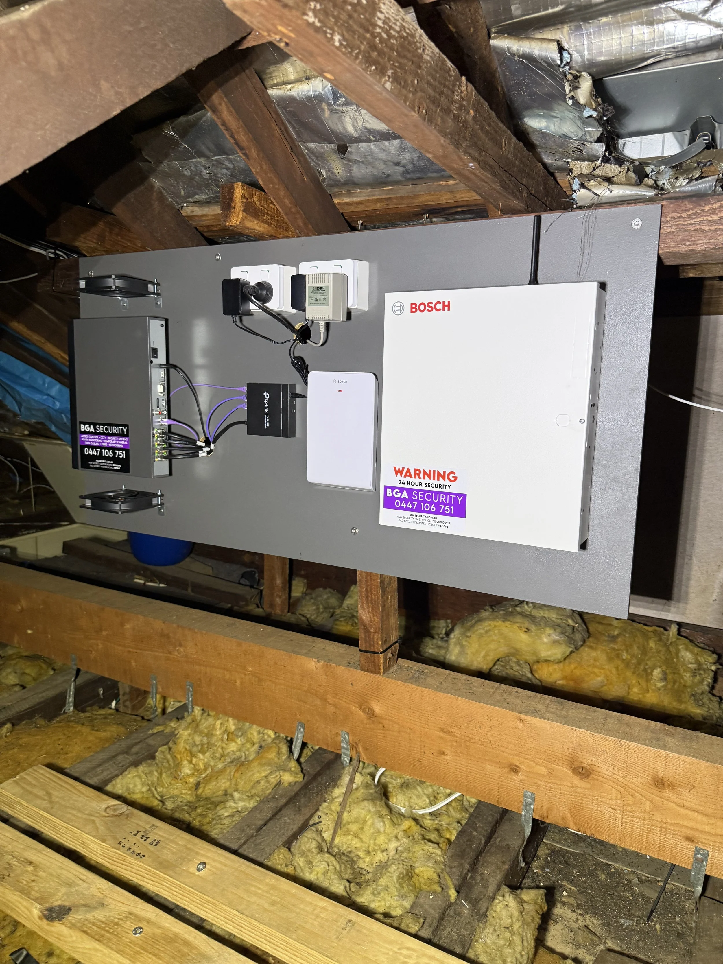 A security panel installed in a roof with an alarm panel, RF receiver, NVR and network switch.