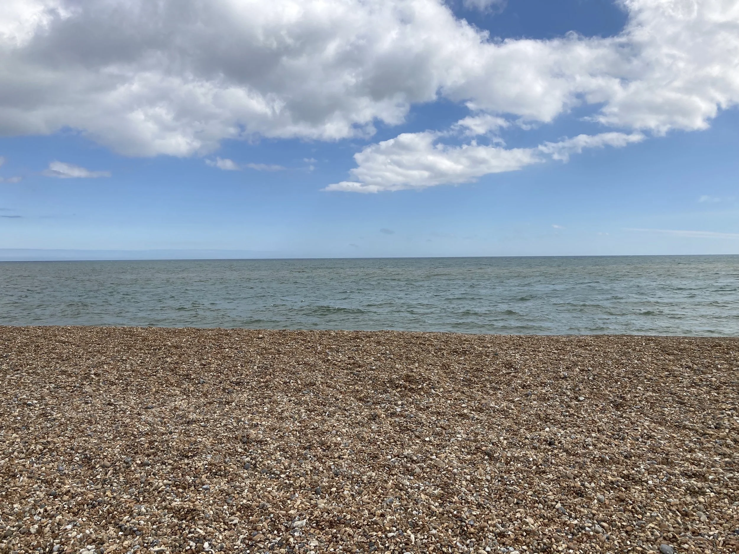 Pebble beach by the ocean with partly cloudy sky.