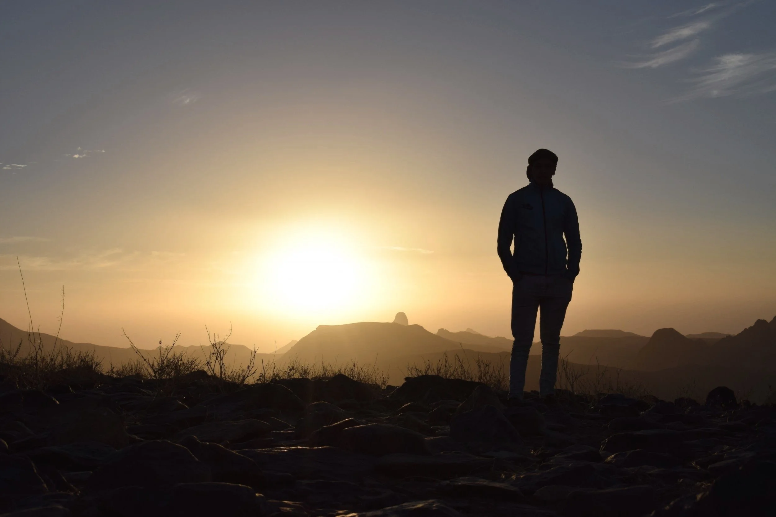Silhouette of a person against a sunrise with mountains in the background.