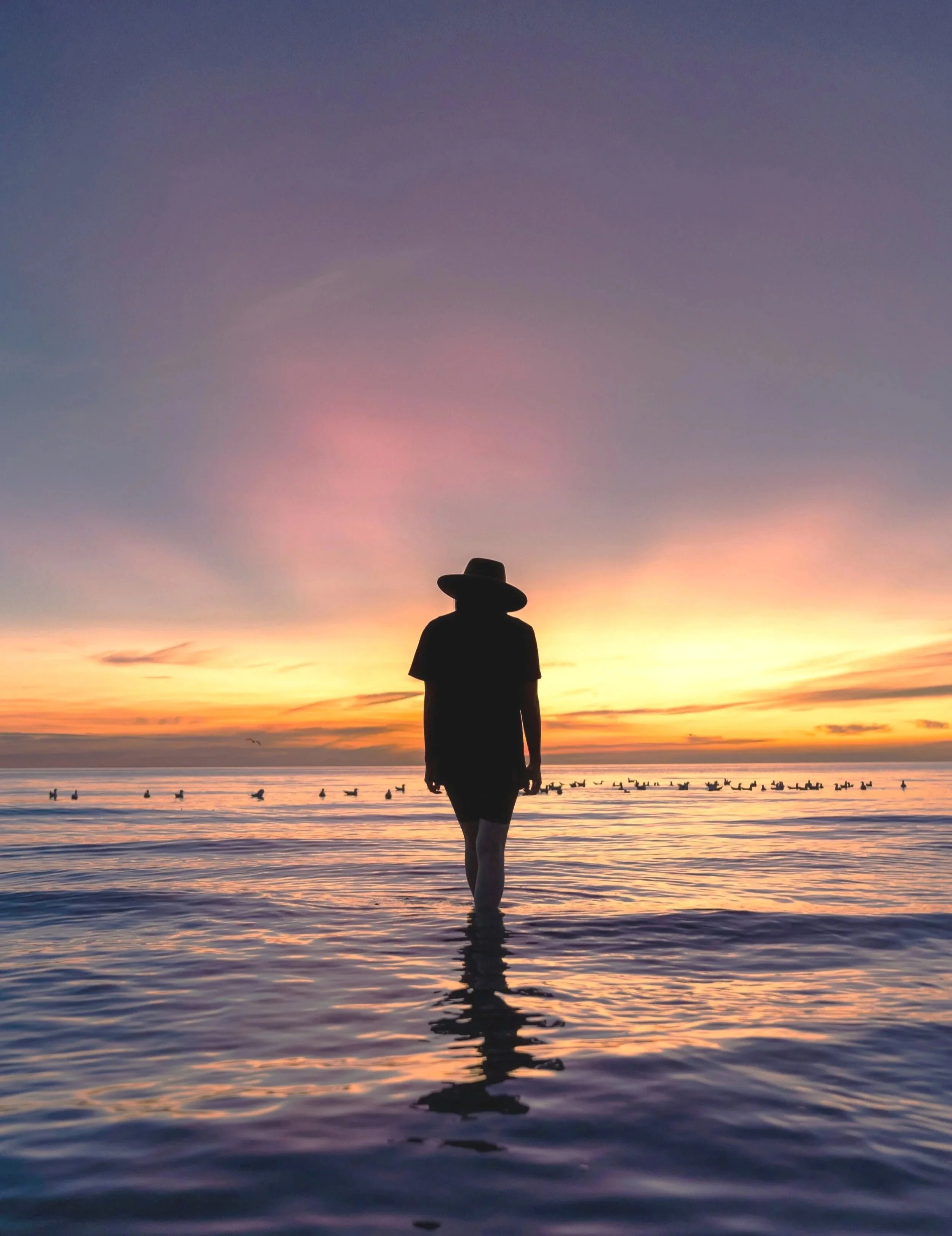 Silhouette of a woman wearing a hat walking on the beach at sunset with a colourful sky