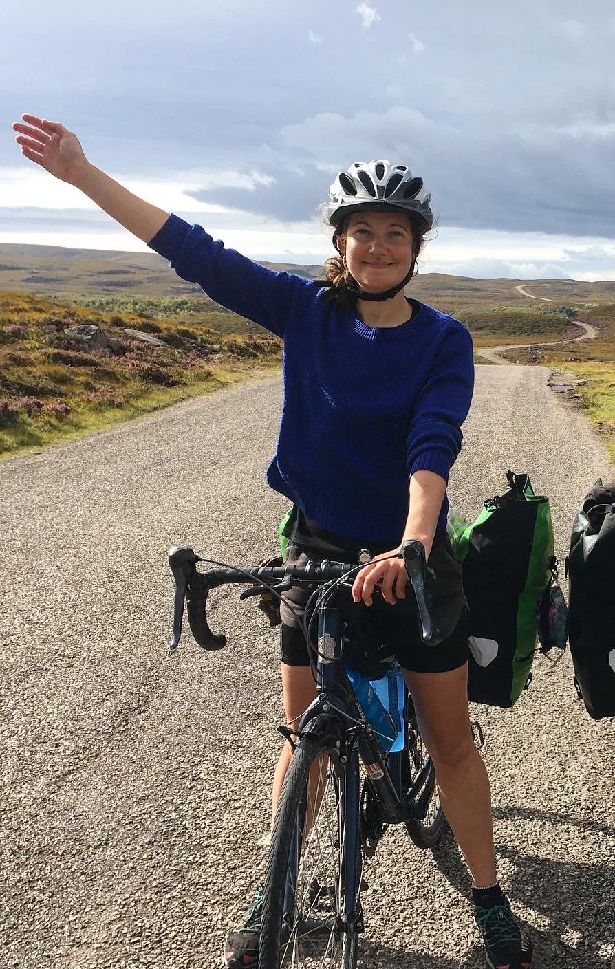 Holly smiles with her bike holding up her right hand
