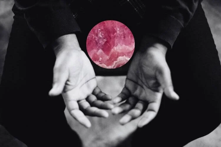 two hands held uplifted in prayer above their lap. a pink crystal sphere collaged between them
