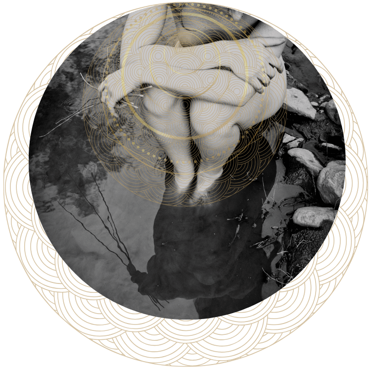 a sepia-tone photo of muse sitting in a shallow river, her arms are resting over her knees. she holds several shoots of horsetail in one hand