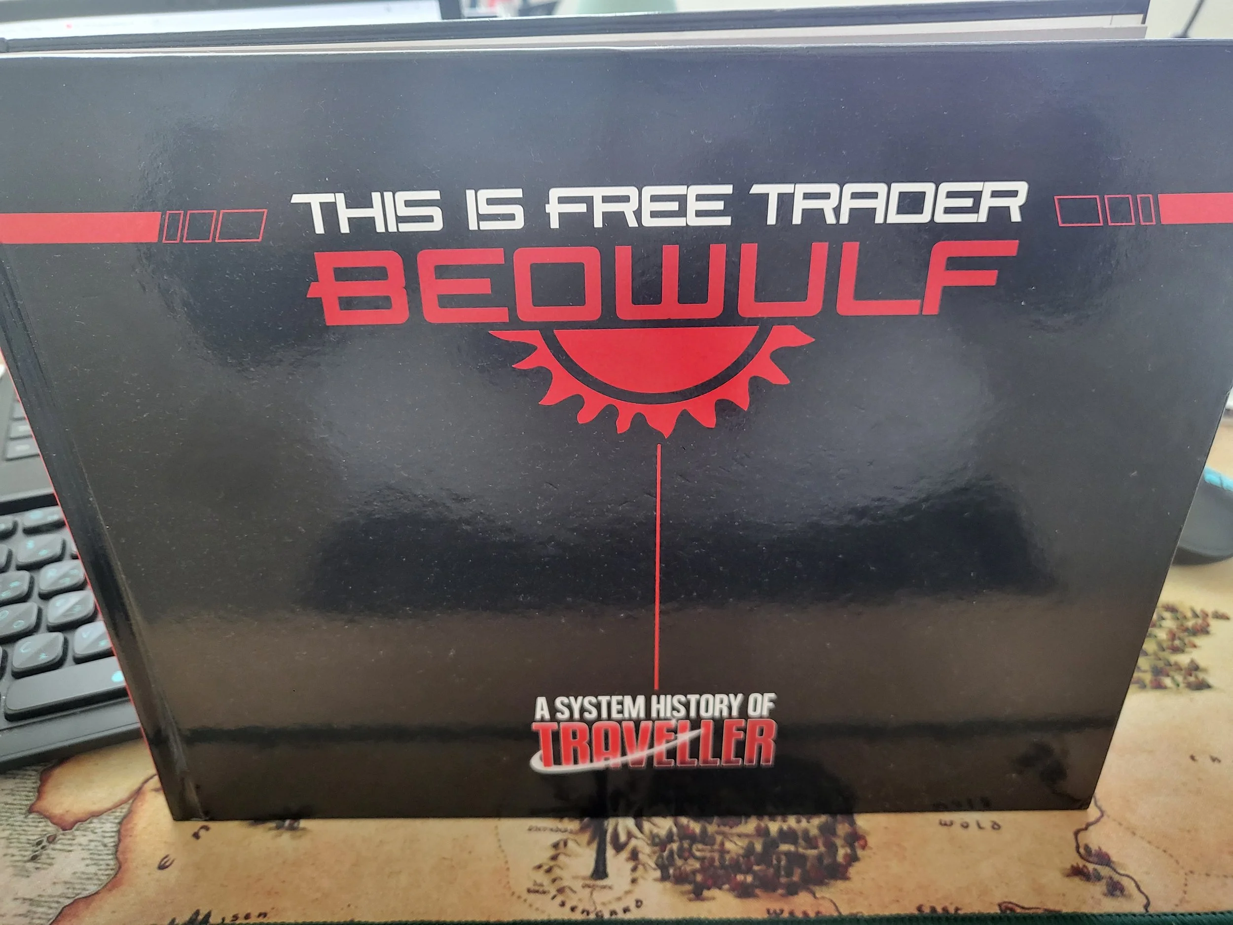 The cover of This is Free Trader Beowulf, which is a minimalist black cover with the text in red and white and the text "A System History of Traveller" in Traveller-esque font at the bottom. It's a big rectangle of a book as well.
