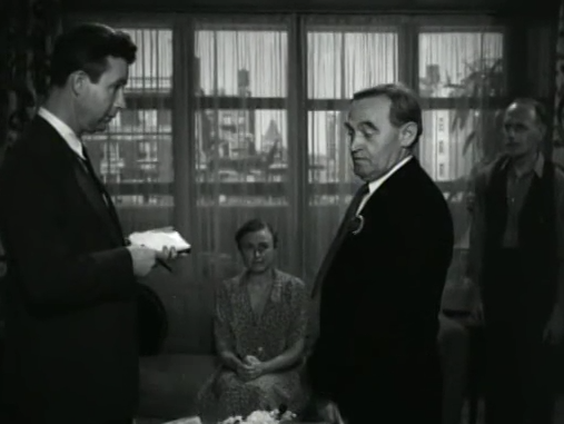 We're in an apartment, the NYC skyline in the windows. On the left is one detective with a notebook, in the center a middle aged lady is sitting down in the background, on the right is an old Irish lad detective, and in the far right is another man