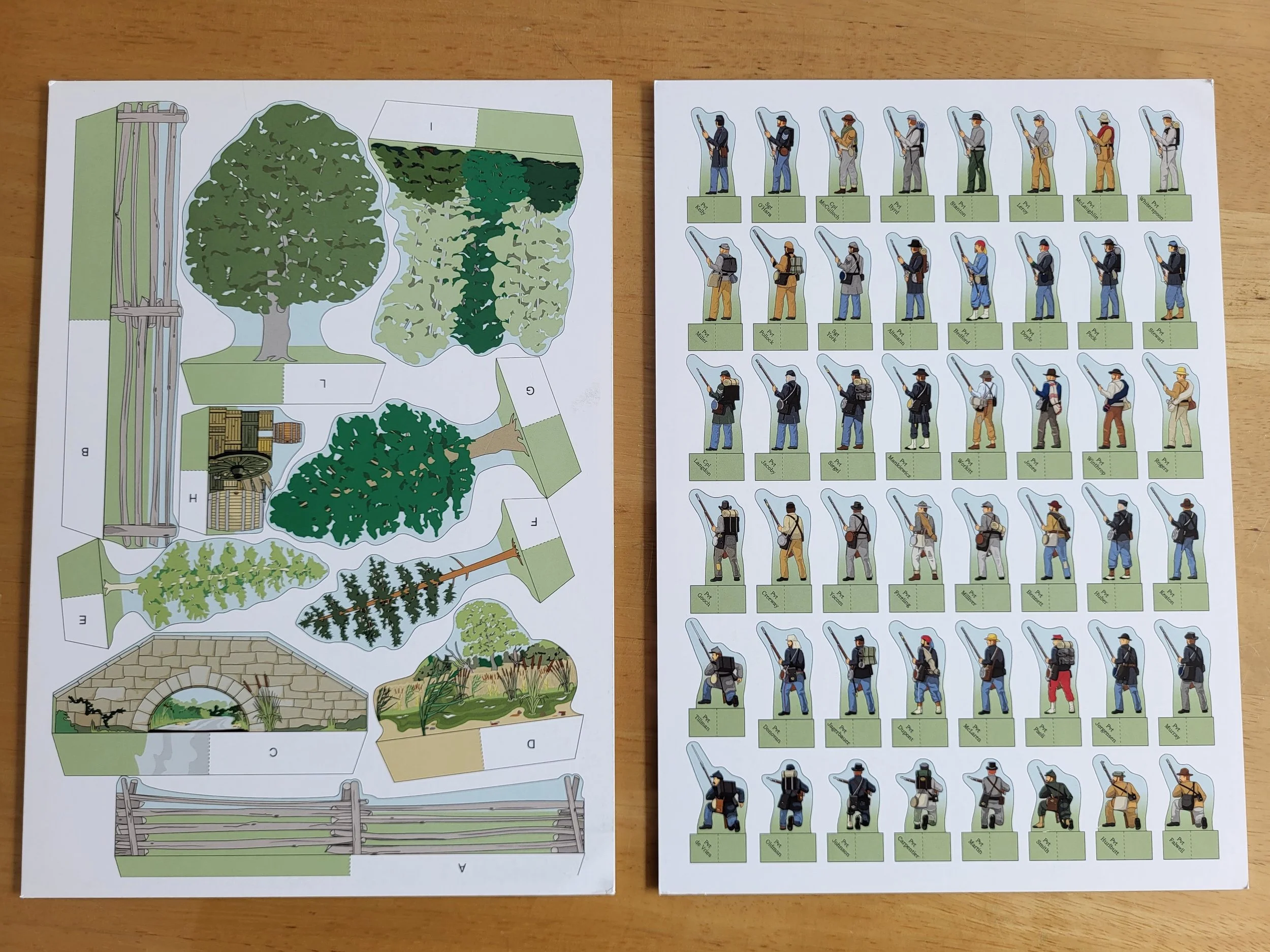 Two pieces of paper. On the left has cut outs showing trees, fences, and a bridge which you can cut out and assemble into terrain. On the right are silhouettes of several dozen soldiers to be cut out and assembled for play.