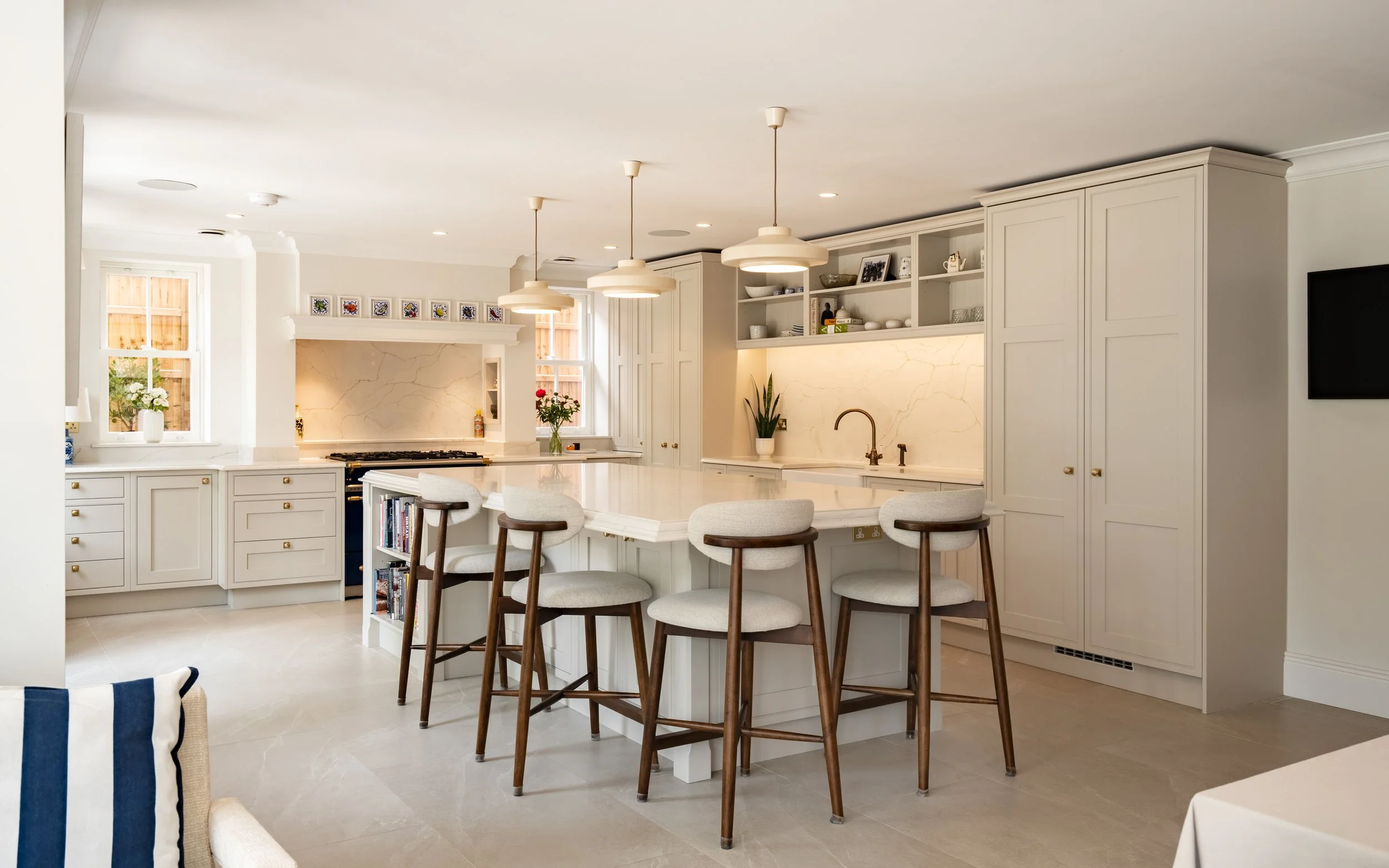 Bright modern kitchen with white cabinetry, marble backsplash, kitchen island with white countertop, five pendant lights, and a built-in oven.