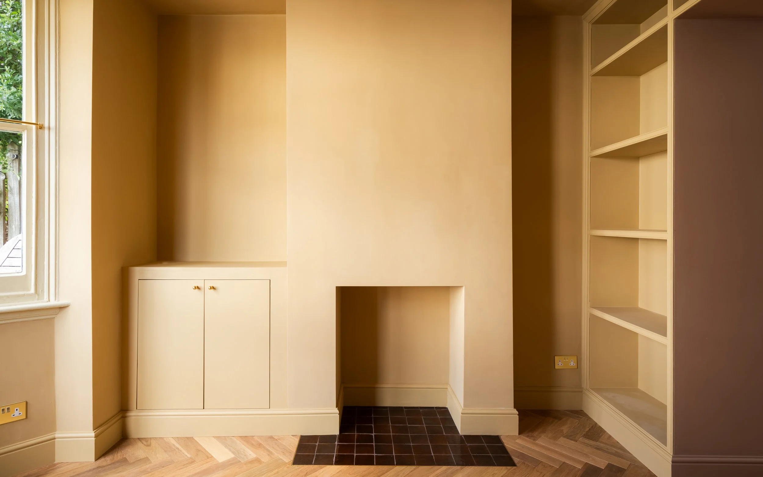 Empty built-in cream-colored cabinets and open shelving in a room with a window, wood flooring, and tiled area.