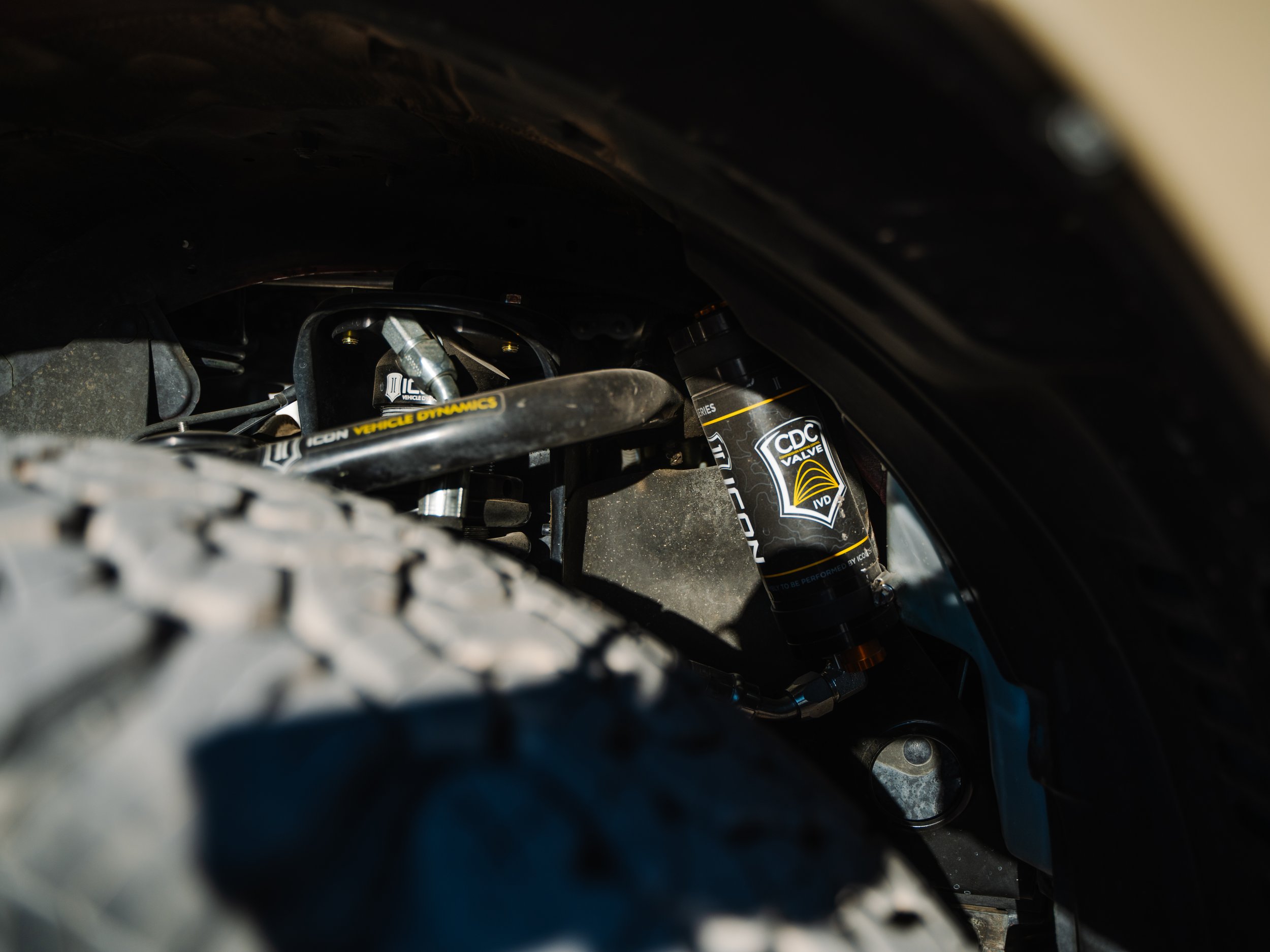Close-up of a vehicle's suspension system showing a Coilover Shock Absorber with CDC Valve branding and a tire tread in the foreground.