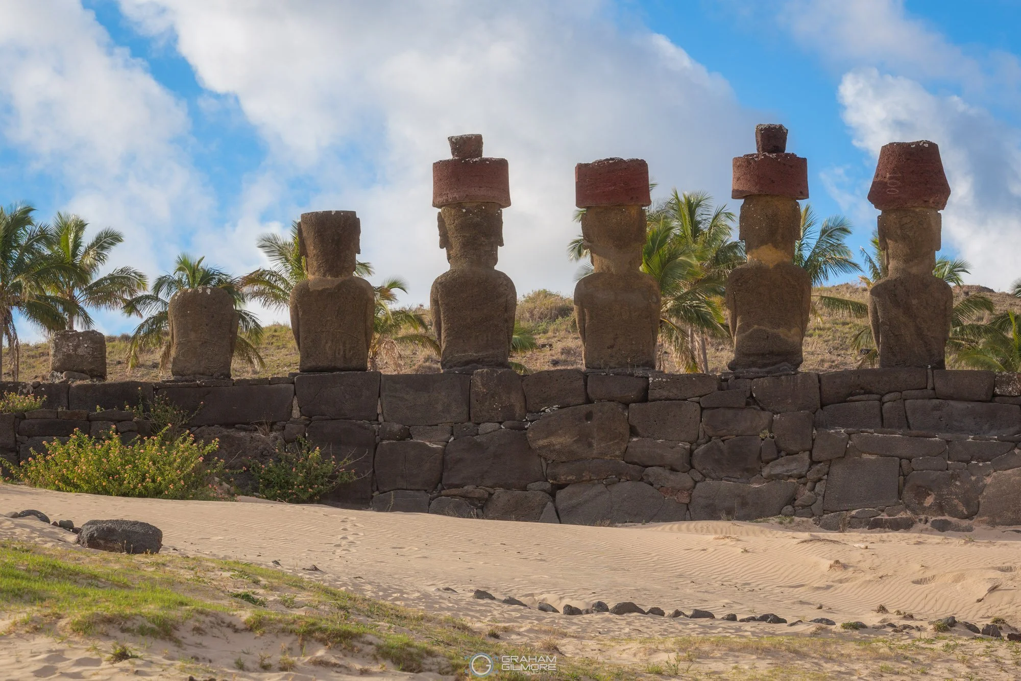 Restored Moai statues at Anakena Beach with palm trees and volcanic landscape in the background on Easter Island