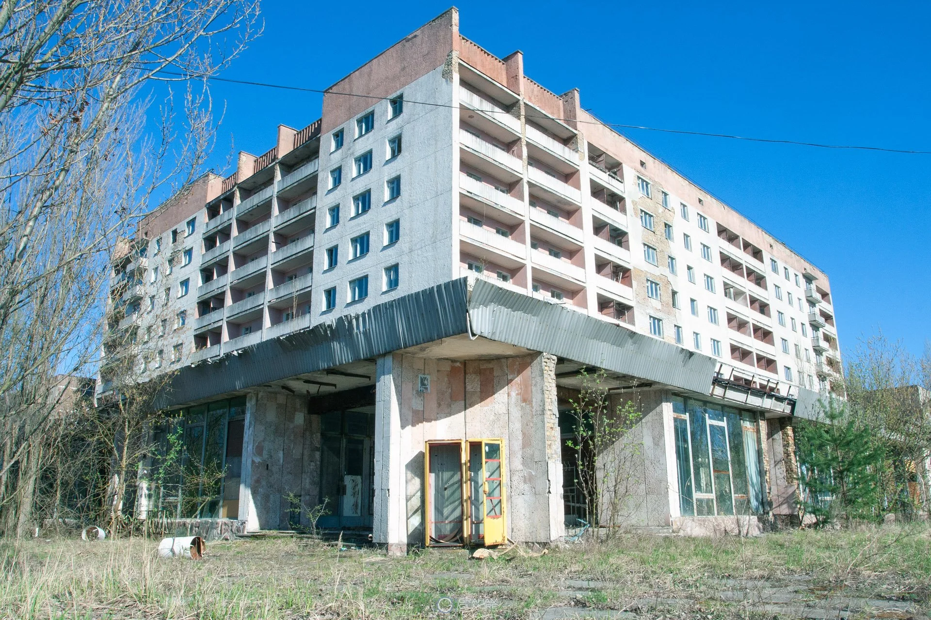 Abandoned multi-story building with a worn exterior, broken windows, and overgrown grass in the foreground.