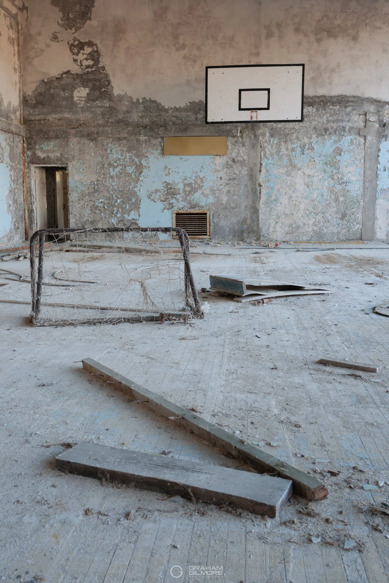 abandoned gymnasium in Pripyat with broken basketball hoop and debris on floor