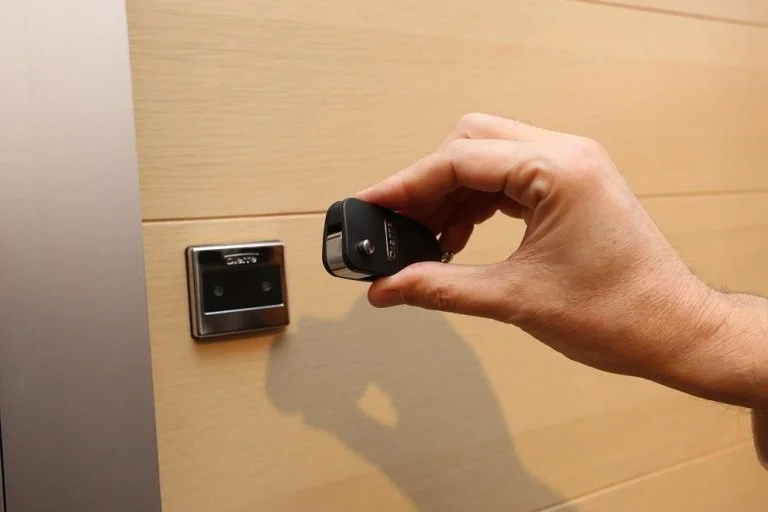 Una mano che sta usando un rilevatore di metalli vicino a una presa Bluetooth su una parete di legno.
