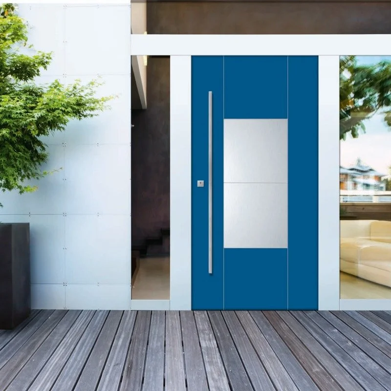 Porta d'ingresso moderna di colore blu con maniglia lunga, vicino a una parete bianca, con una finestra a destra e un'area soggiorno visibile dietro.