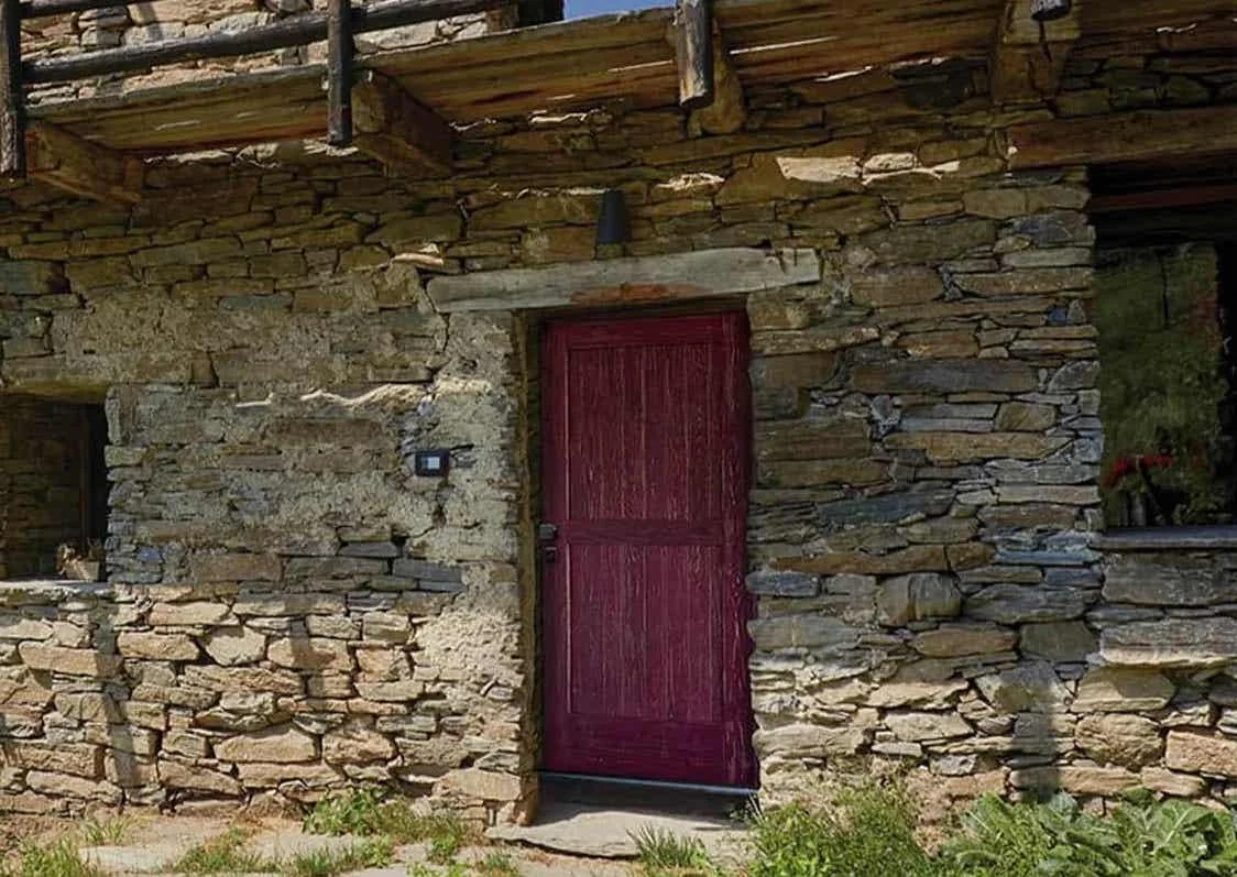 Porta di legno rossa in una parete in pietra di una casetta di campagna.