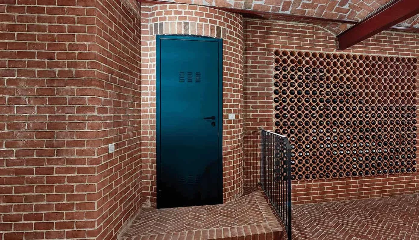 Paredes di mattoni rossi, porta blu in metallo, parete di tubi di terracotta disposti a rete, ringhiera nera con scala.
