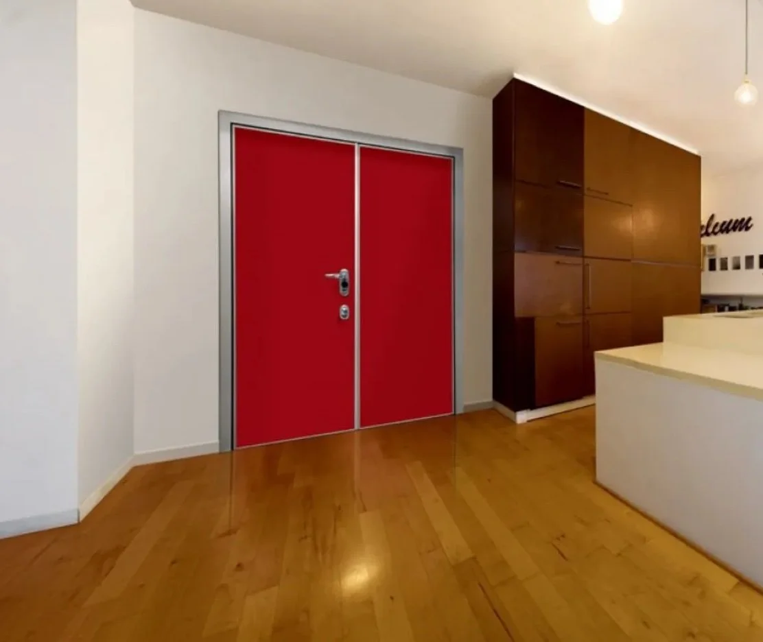 Porta rossa con maniglia e serratura in un ambiente con pareti bianche, pavimento in legno e armadio in legno scuro.