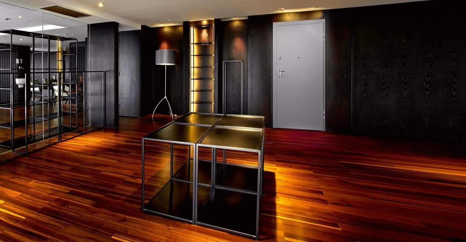 Interno di un spazio moderno con pareti nere, pavimento in legno, scaffale in metallo nero, lampada da terra grigia, parete con luci soffuse e porta bianca.