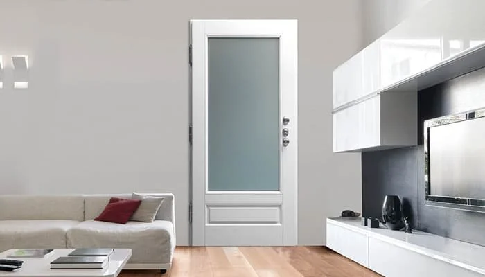 Soggiorno moderno con porta bianca, divano beige con cuscino rosso, televisore e mensole bianche