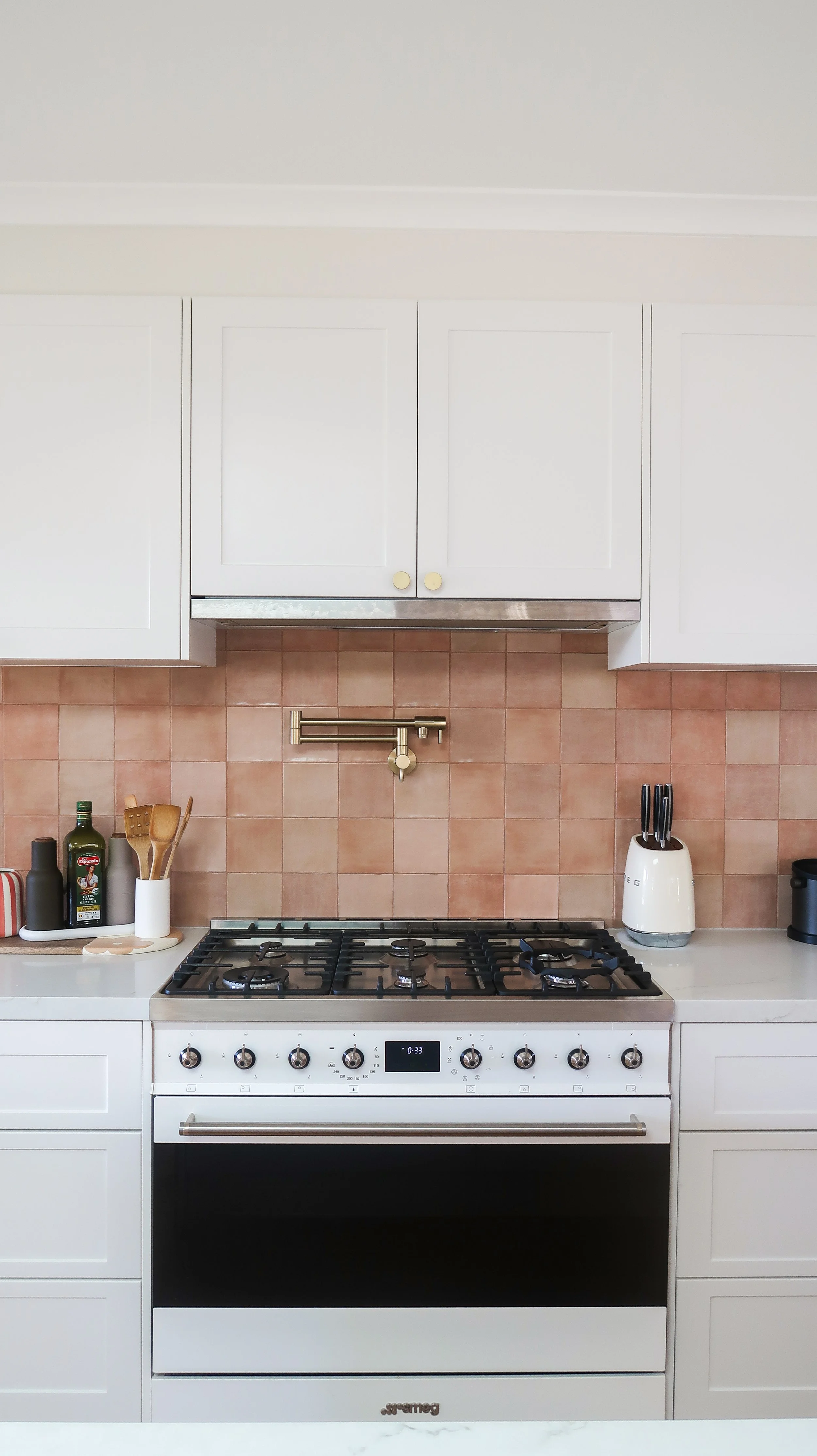 White kitchen stove with four burners, beige tile backsplash, white cabinets, and small kitchen appliances on the counter.